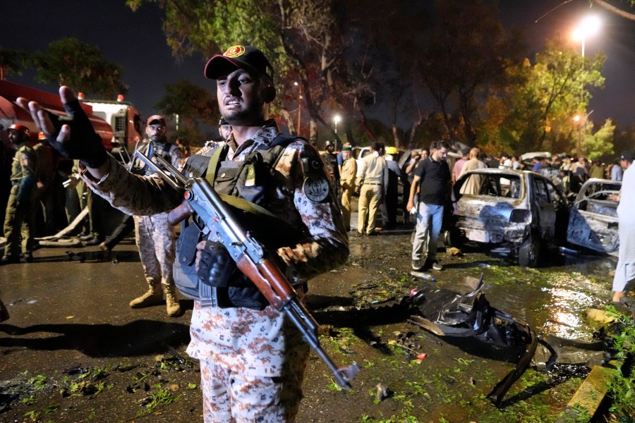 A paramilitary soldier gestures toward media as security officials examine the site of an explosion that caused injures and destroyed vehicles at outside the Karachi airport, Pakistan, Monday, Oct. 7, 2024. (AP Photo/Fareed Khan)