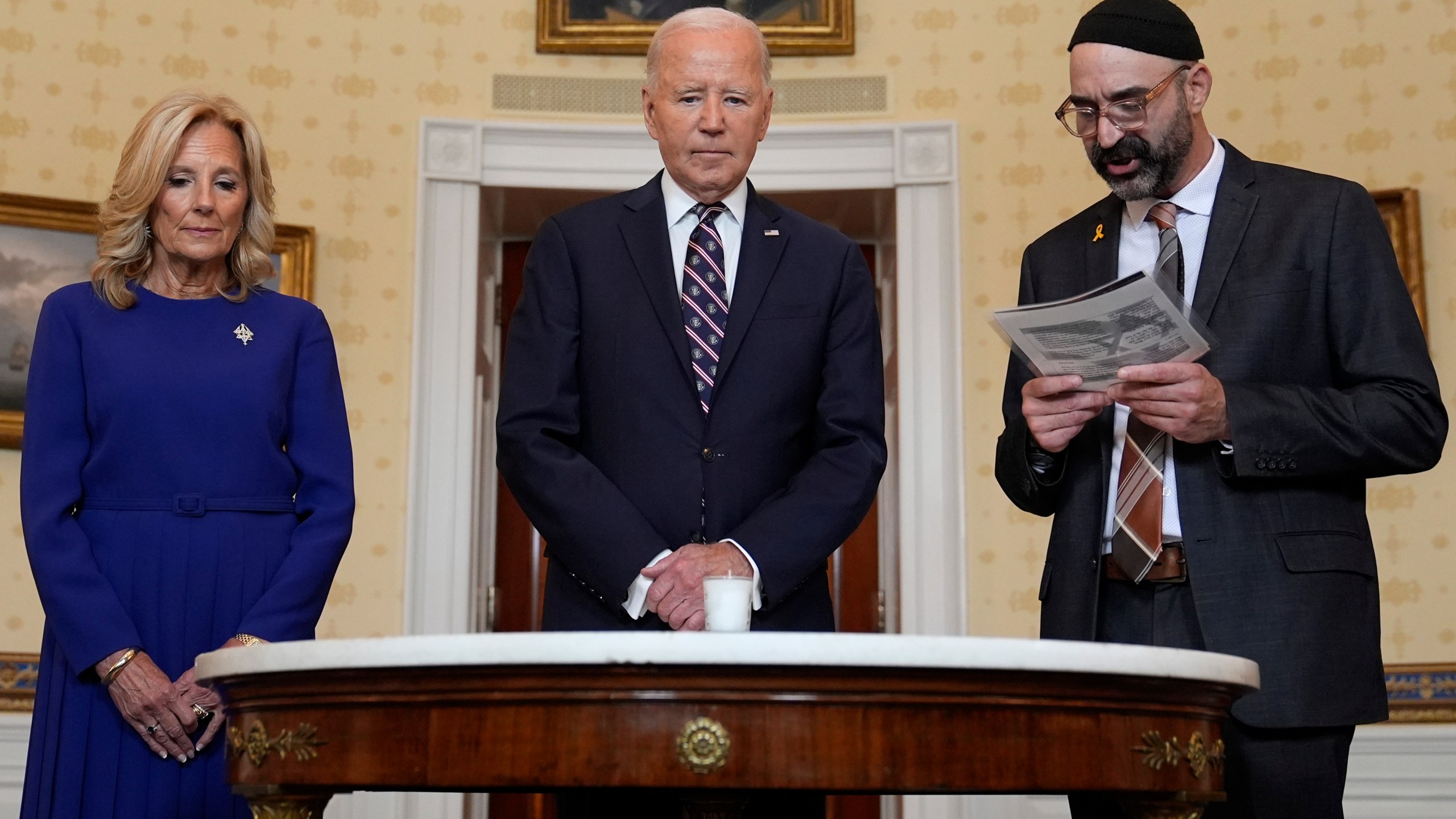 President Joe Biden, center, standing with first lady Jill Biden, left, and Rabbi Aaron Alexander of the Adas Israel Congregation, participates in a memorial candle-lighting in the Blue Room of the White House in Washington, Monday, Oct. 7, 2024, to mark the one-year anniversary of the Hamas attack on Israel that left about 1,200 people dead. (AP Photo/Susan Walsh)