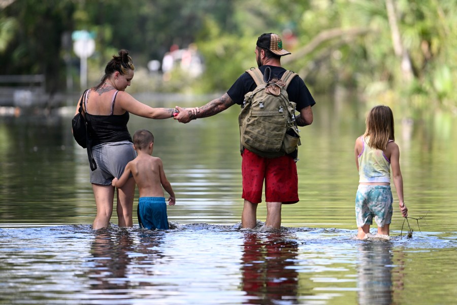 FILE - Dustin Holmes, second from right, holds hands with his girlfriend, Hailey Morgan, while returning to their flooded home with her children Aria Skye Hall, 7, right, and Kyle Ross, 4, in the aftermath of Hurricane Helene, Sept. 27, 2024, in Crystal River, Fla. (AP Photo/Phelan M. Ebenhack, File)