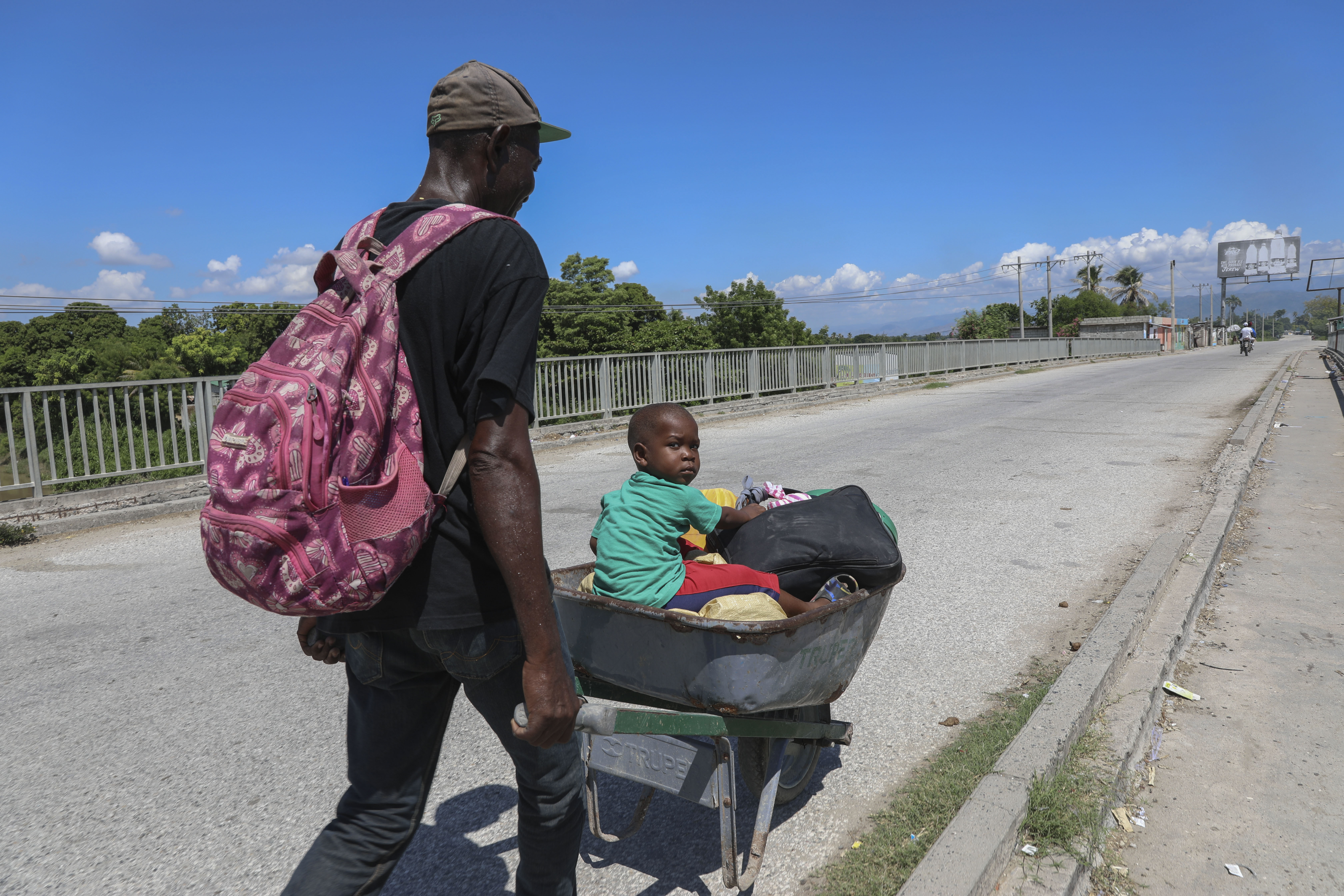 A man pushes a child in a wheelbarrow along a street in Pont-Sonde, Haiti, Monday, Oct. 7, 2024, days after a gang attacked the town. (AP Photo/Odelyn Joseph)