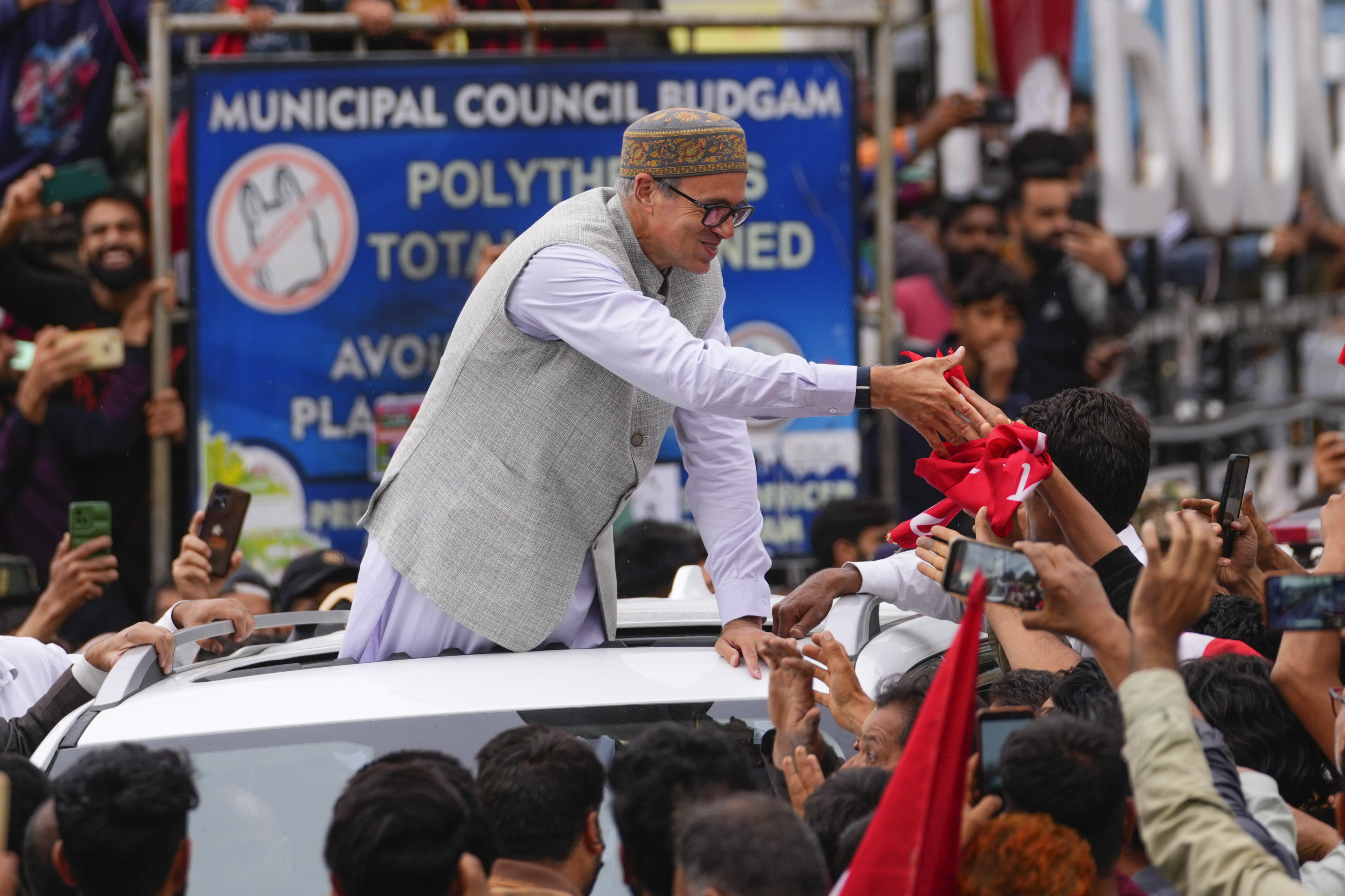 Jammu and Kashmir National Conference (JKNC) party leader Omar Abdullah, standing in car shakes hands with supporters as he celebrates his victory in the election for a local government in Indian controlled Kashmir, Budgam, Tuesday, Oct. 8, 2024. (AP Photo/Dar Yasin)