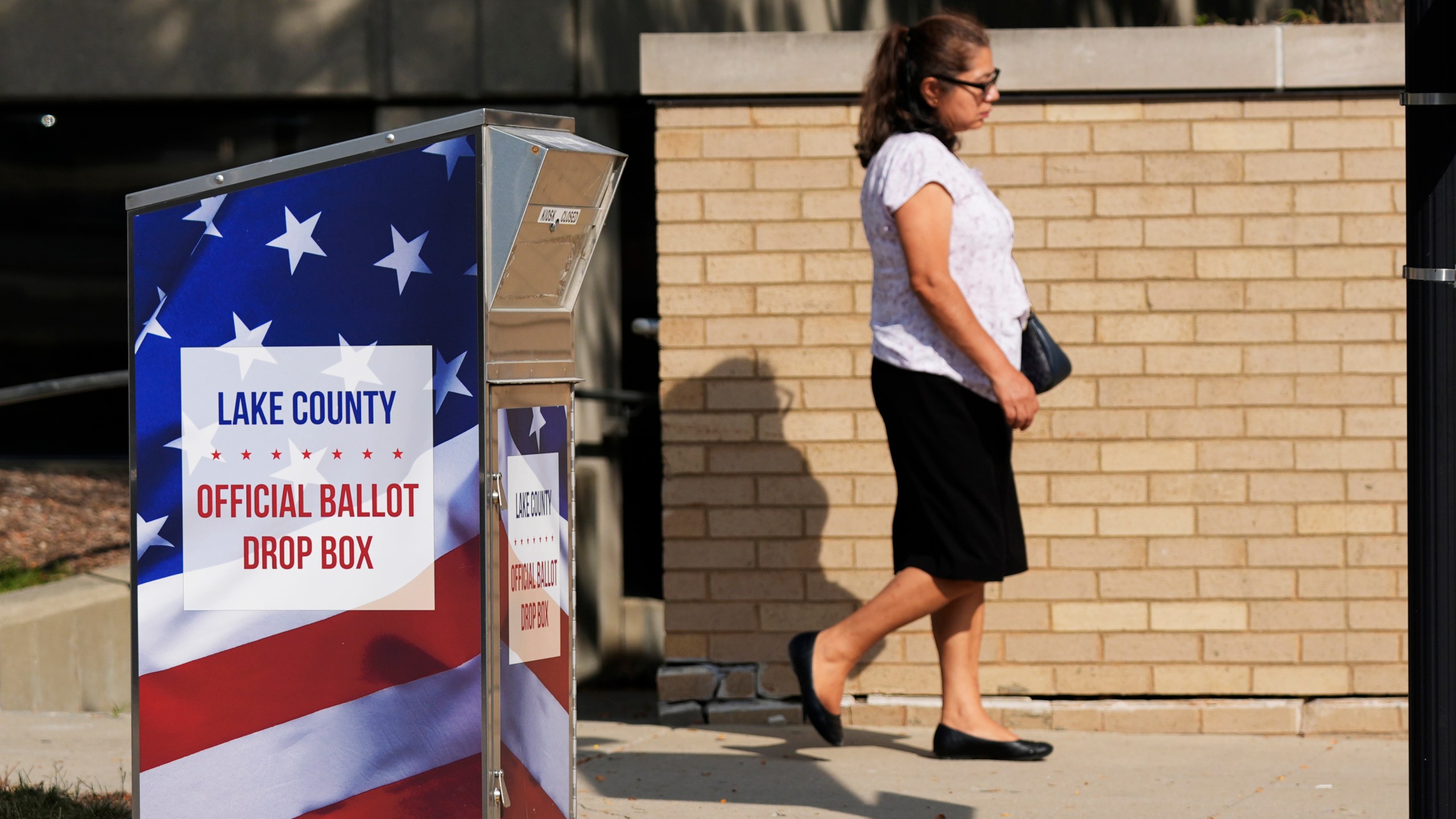 A person walks past a ballot drop-box for Lake County in downtown Waukegan in Waukegan, Ill., Monday, Sept. 16, 2024. (AP Photo/Nam Y. Huh)