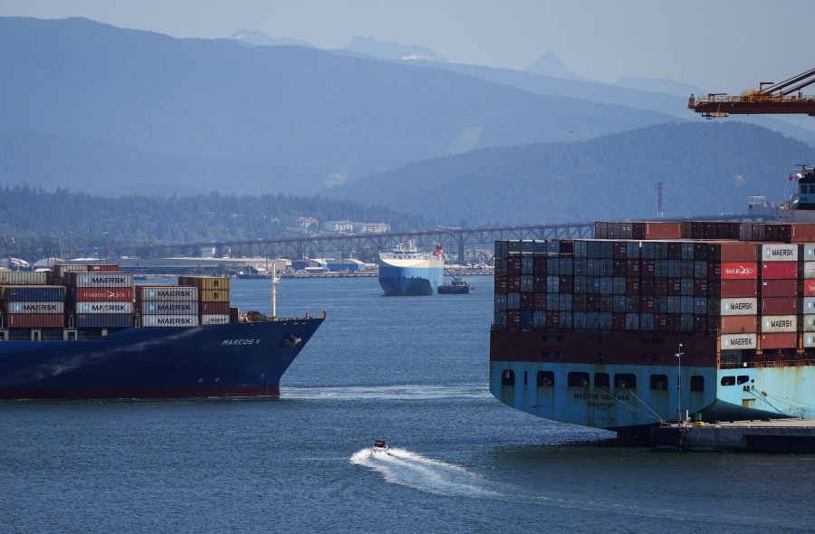 FILE - A boater passes between cargo ships on the harbor, in Vancouver, British Columbia, July 16, 2024. (Darryl Dyck/The Canadian Press via AP, File)