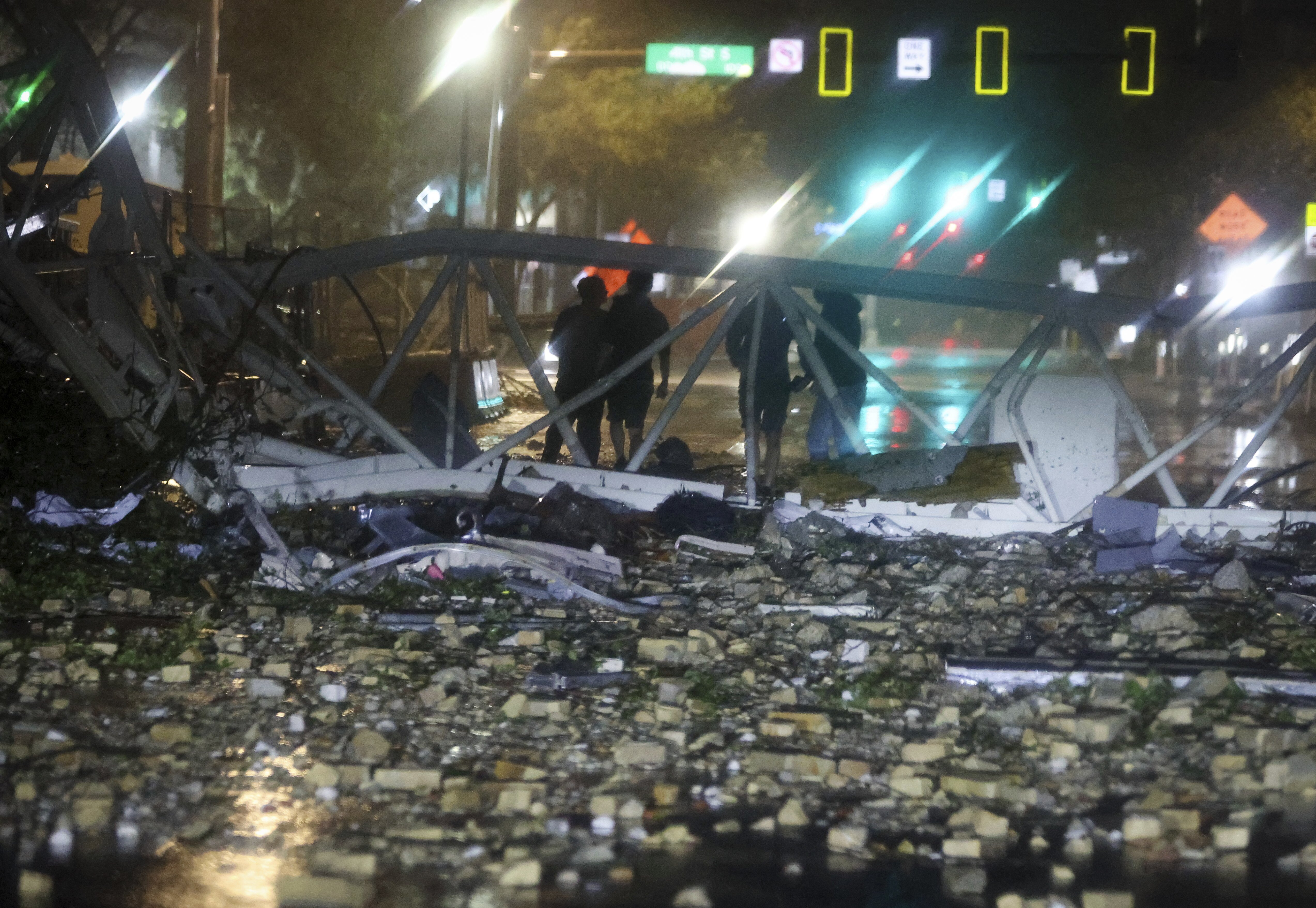 A group is silhouetted against a fallen crane along 1st Avenue South near the Tampa Bay Times offices in St. Petersburg, Florida, Thursday, Oct. 10, 2024, as Hurricane Milton's strong winds tore through the area. (Chris Urso/Tampa Bay Times via AP)