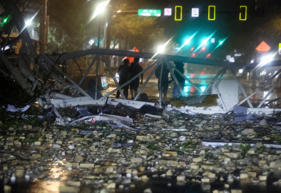 A group is silhouetted against a fallen crane along 1st Avenue South near the Tampa Bay Times offices in St. Petersburg, Florida, Thursday, Oct. 10, 2024, as Hurricane Milton's strong winds tore through the area. (Chris Urso/Tampa Bay Times via AP)