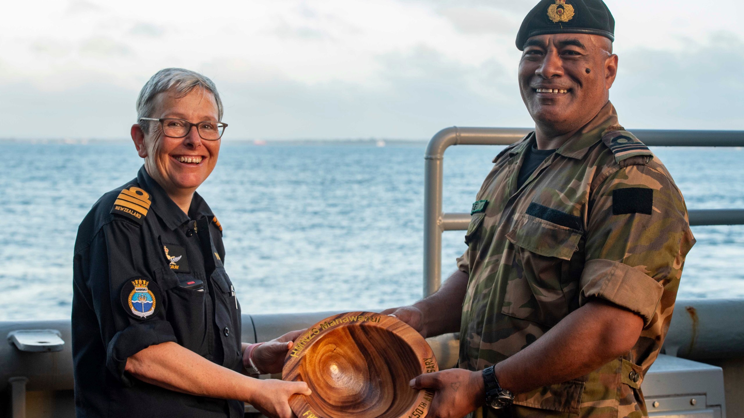 In this undated photo provided by the New Zealand Defence Force, Lieutenant Commander Tala Mafile'o of the Royal Tongan Navy presents Commander Yvonne Gray, left, with a carved wooden bowl as a memento of the RNZN's participation in the 50th Anniversary Fleet Review. (New Zealand Defence Force via AP)