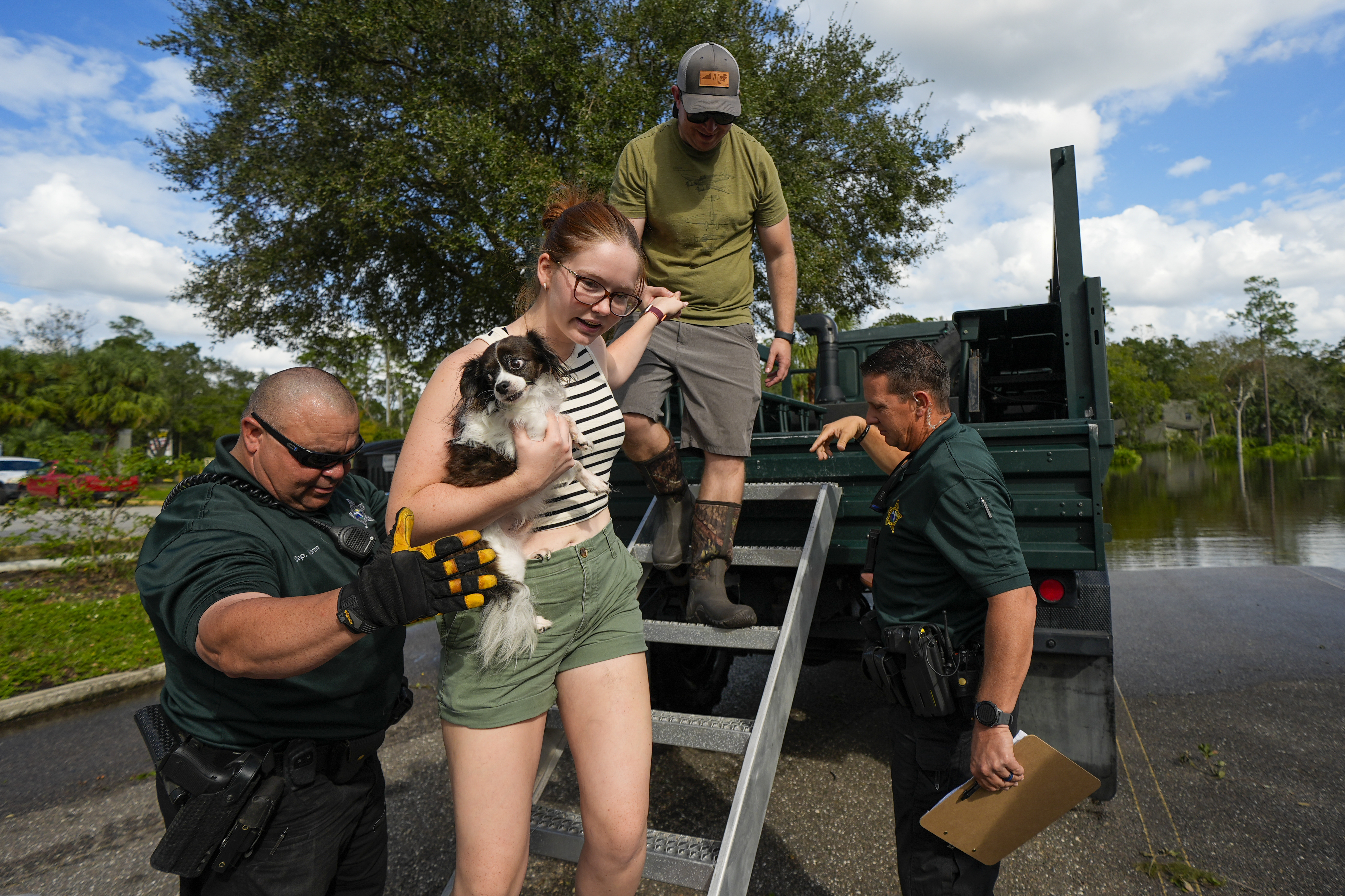 Sarah McRee holds a dog named Poe as she is helped off a high-clearance vehicle by Panellas County Sheriff officials after she was escorted in and out of the Tarpon Woods neighborhood as people return to their homes following Hurricane Milton, Friday, Oct. 11, 2024, in Palm Harbor, Fla. (AP Photo/Julio Cortez)