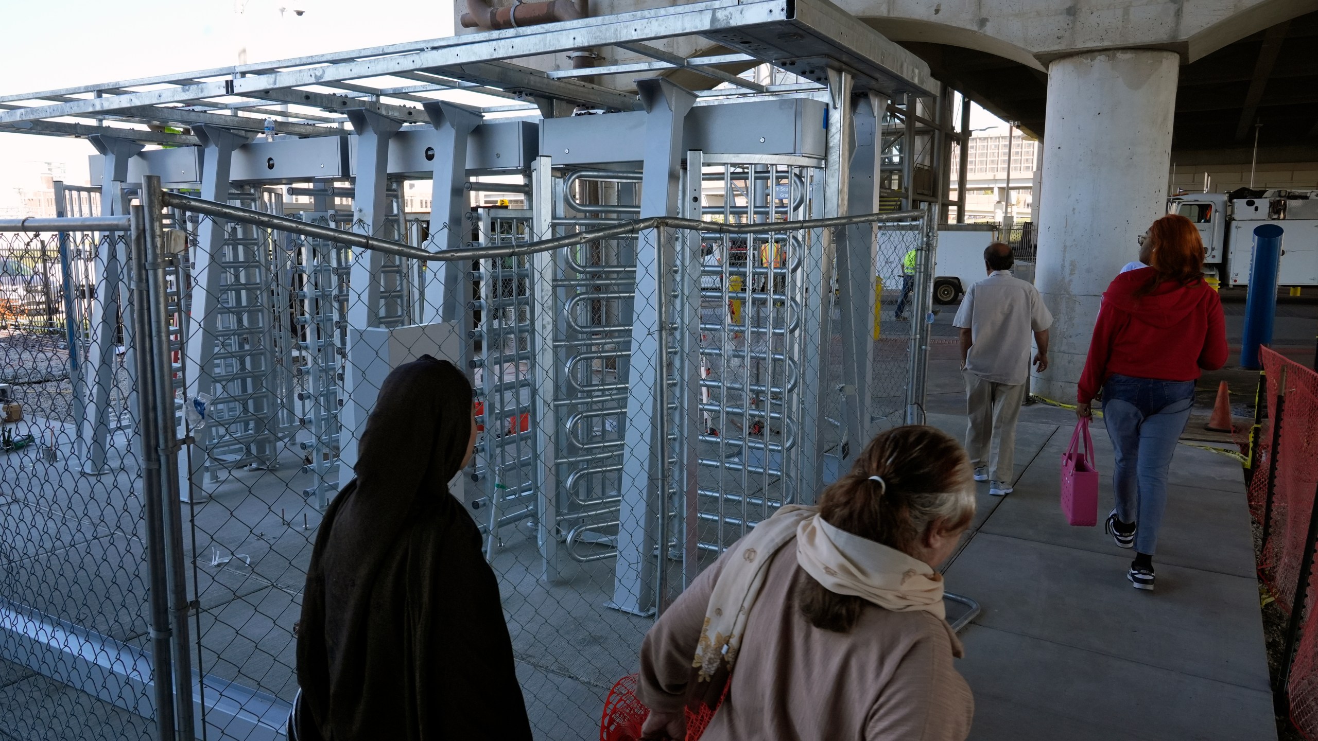 Riders walk around metal gates being installed that will prevent customers from entering a MetroLink platform without a valid fare card Wednesday, Oct. 9, 2024, in St. Louis. (AP Photo/Jeff Roberson)