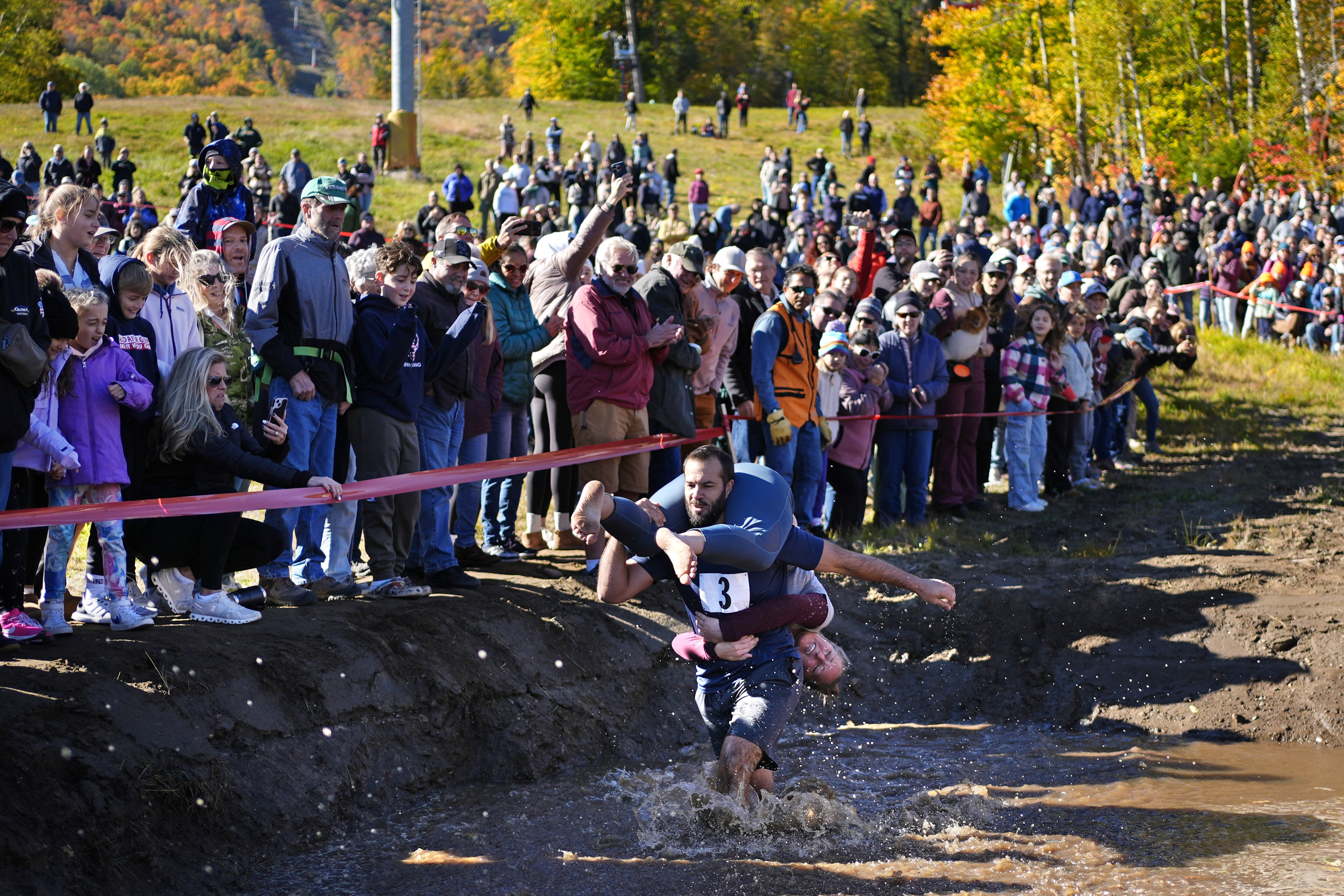 Jon Heaner splashes through the water hazard while carrying Renee Heaner during the North American Wife Carrying Championship, Saturday, Oct. 12, 2024, at Sunday River ski resort in Newry, Maine. (AP Photo/Robert F. Bukaty)