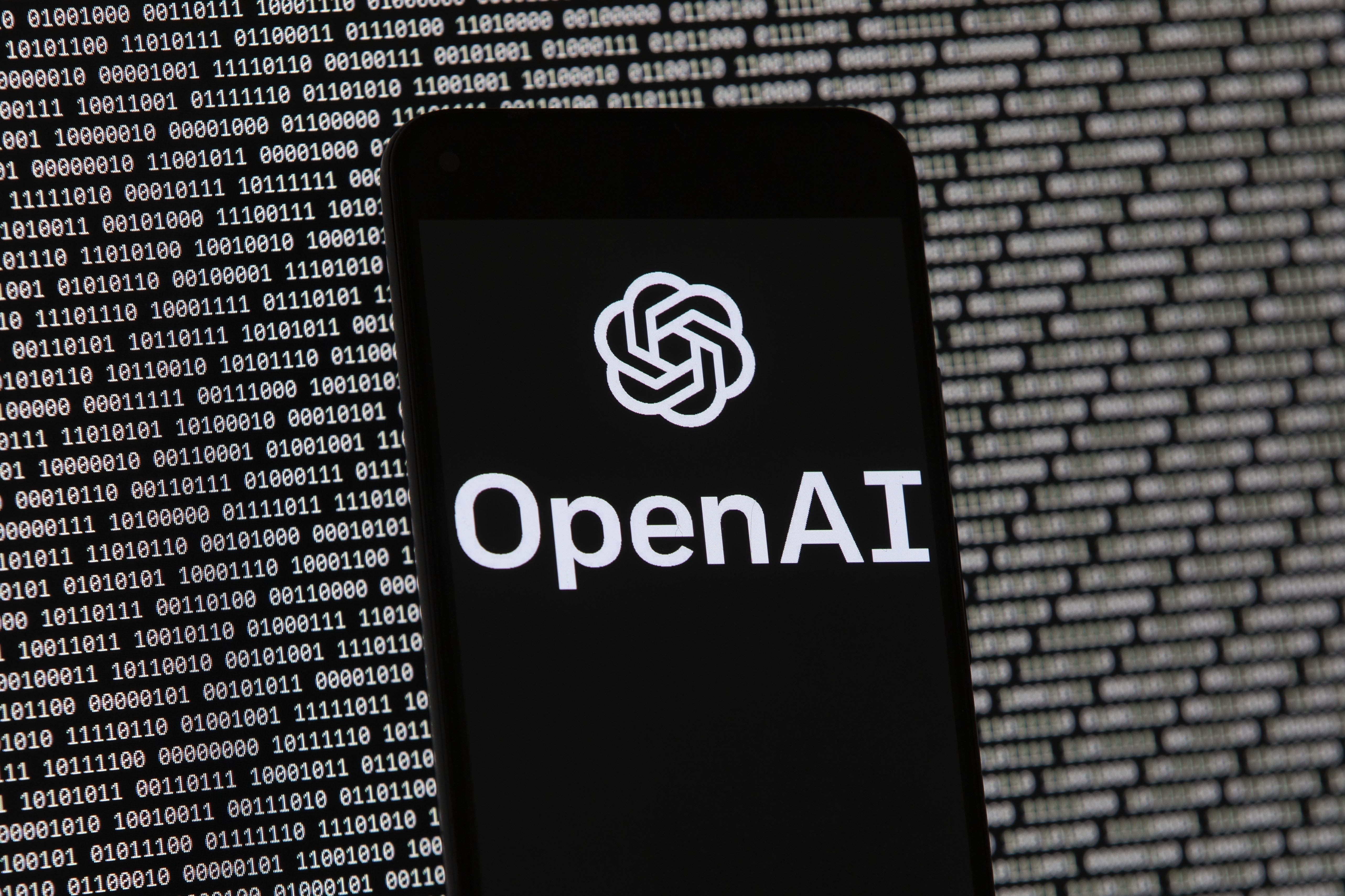 FILE - The OpenAI logo appears on a mobile phone in front of a computer screen with random binary data, March 9, 2023, in Boston. (AP Photo/Michael Dwyer, File)