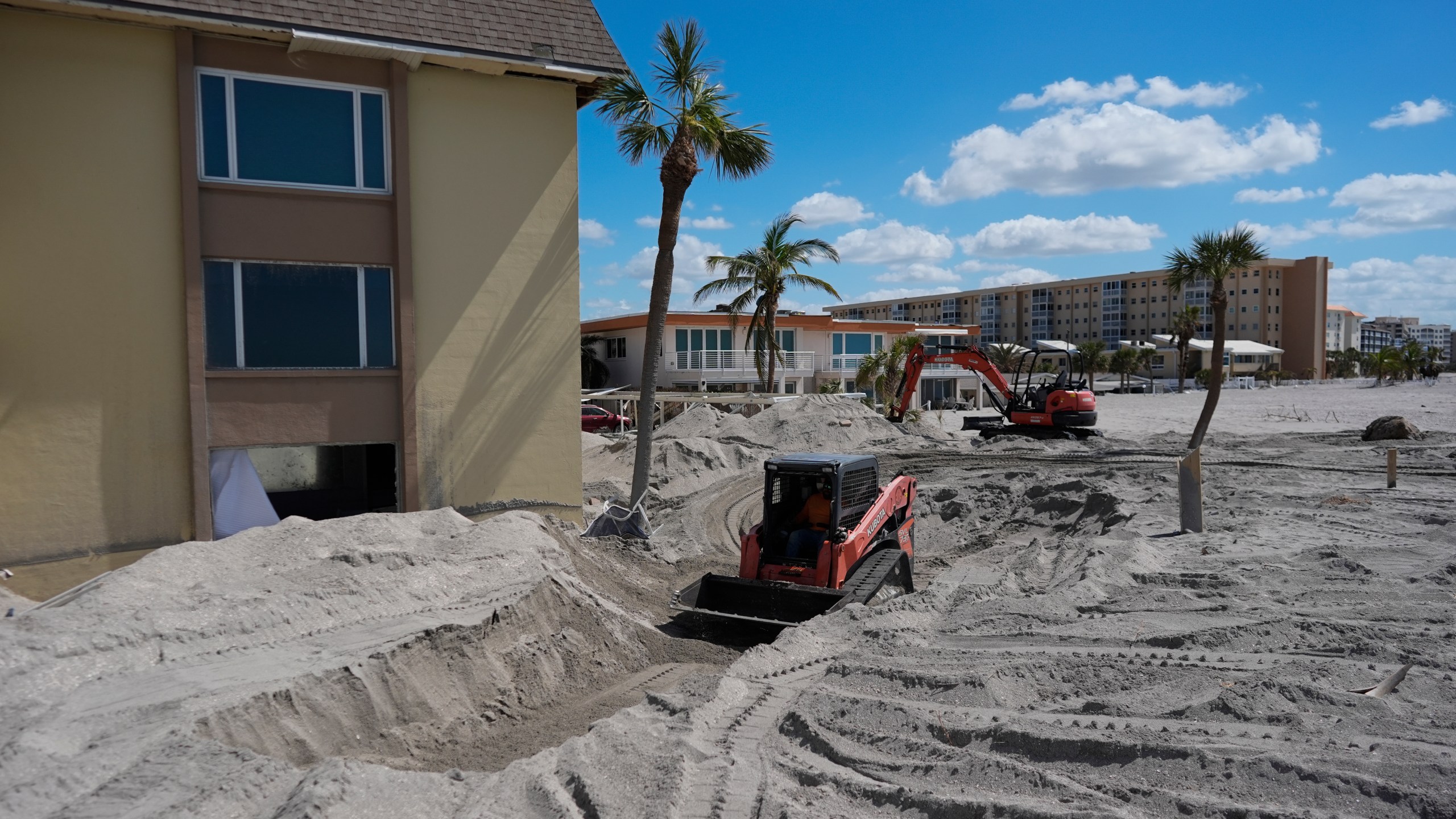 Scott Bennett, a contractor who specializes in storm recovery, drives a skid steer as he removes sand around 5 feet deep from the patio of a beachfront condominium in Venice, Fla., following the passage of Hurricane Milton, Saturday, Oct. 12, 2024. (AP Photo/Rebecca Blackwell)