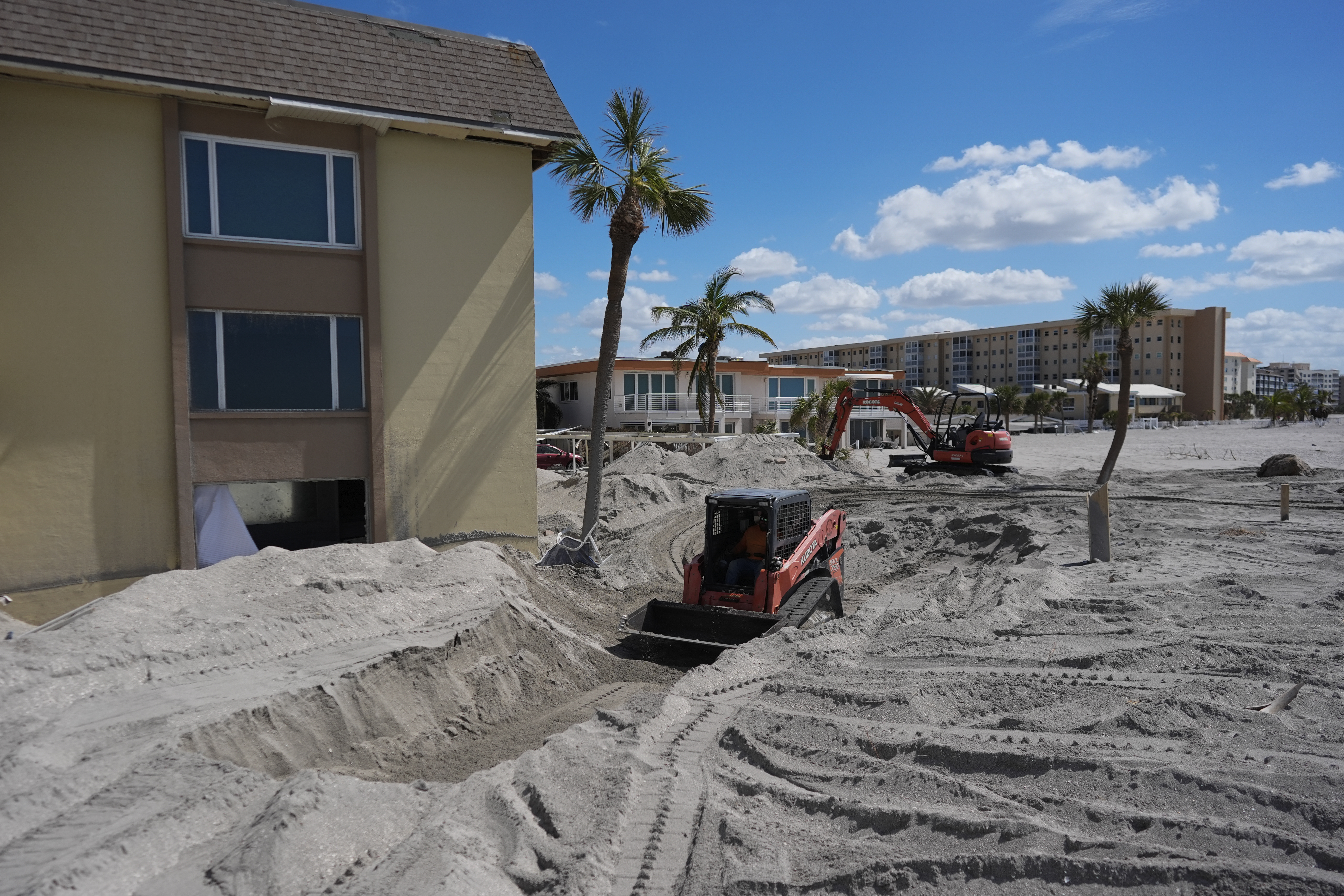 Scott Bennett, a contractor who specializes in storm recovery, drives a skid steer as he removes sand around 5 feet deep from the patio of a beachfront condominium in Venice, Fla., following the passage of Hurricane Milton, Saturday, Oct. 12, 2024. (AP Photo/Rebecca Blackwell)