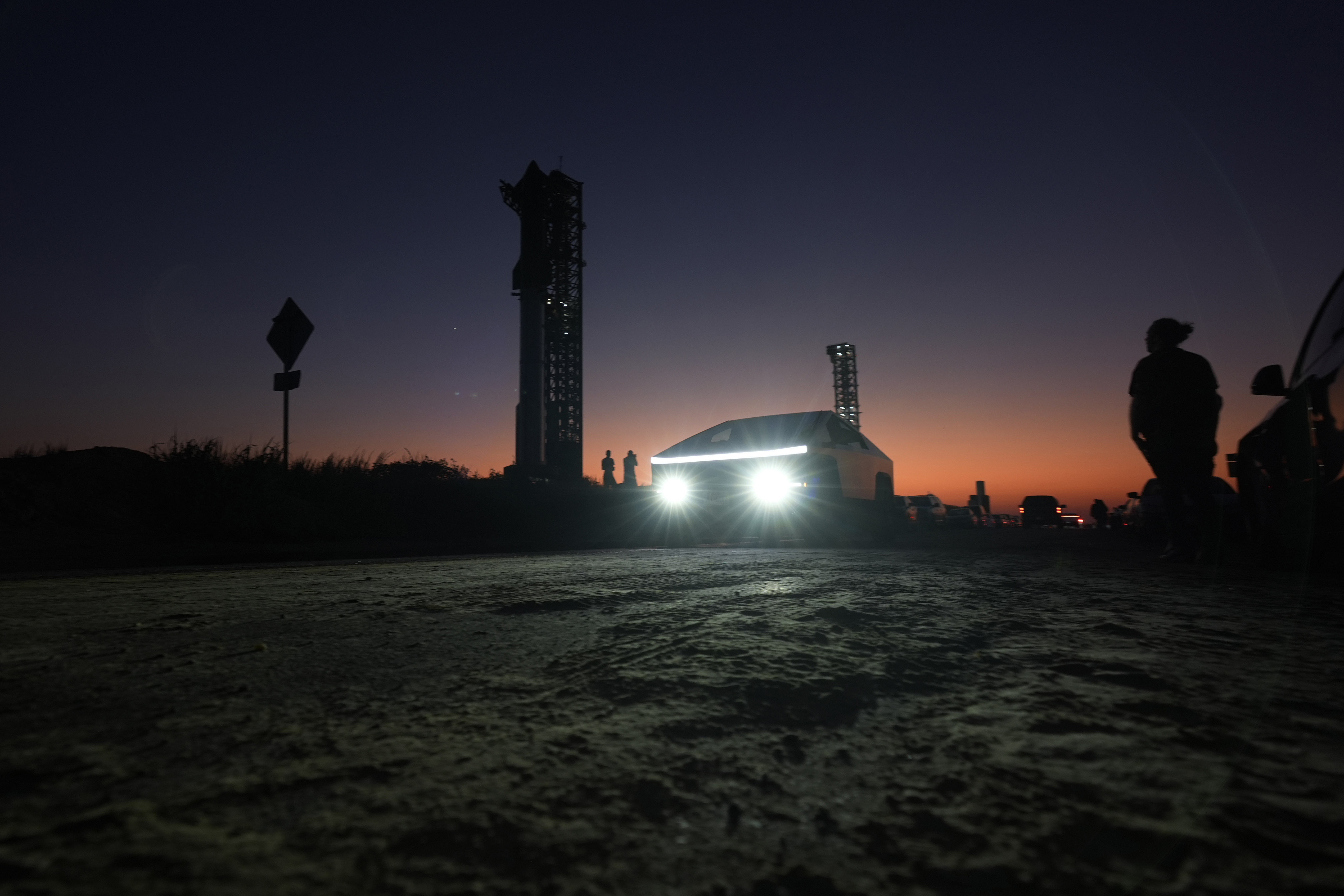 A Tesla Cybertruck passes as the sun sets behind SpaceX's mega rocket Starship, Saturday, Oct. 12, 2024, in Boca Chica, Texas. (AP Photo/Eric Gay)