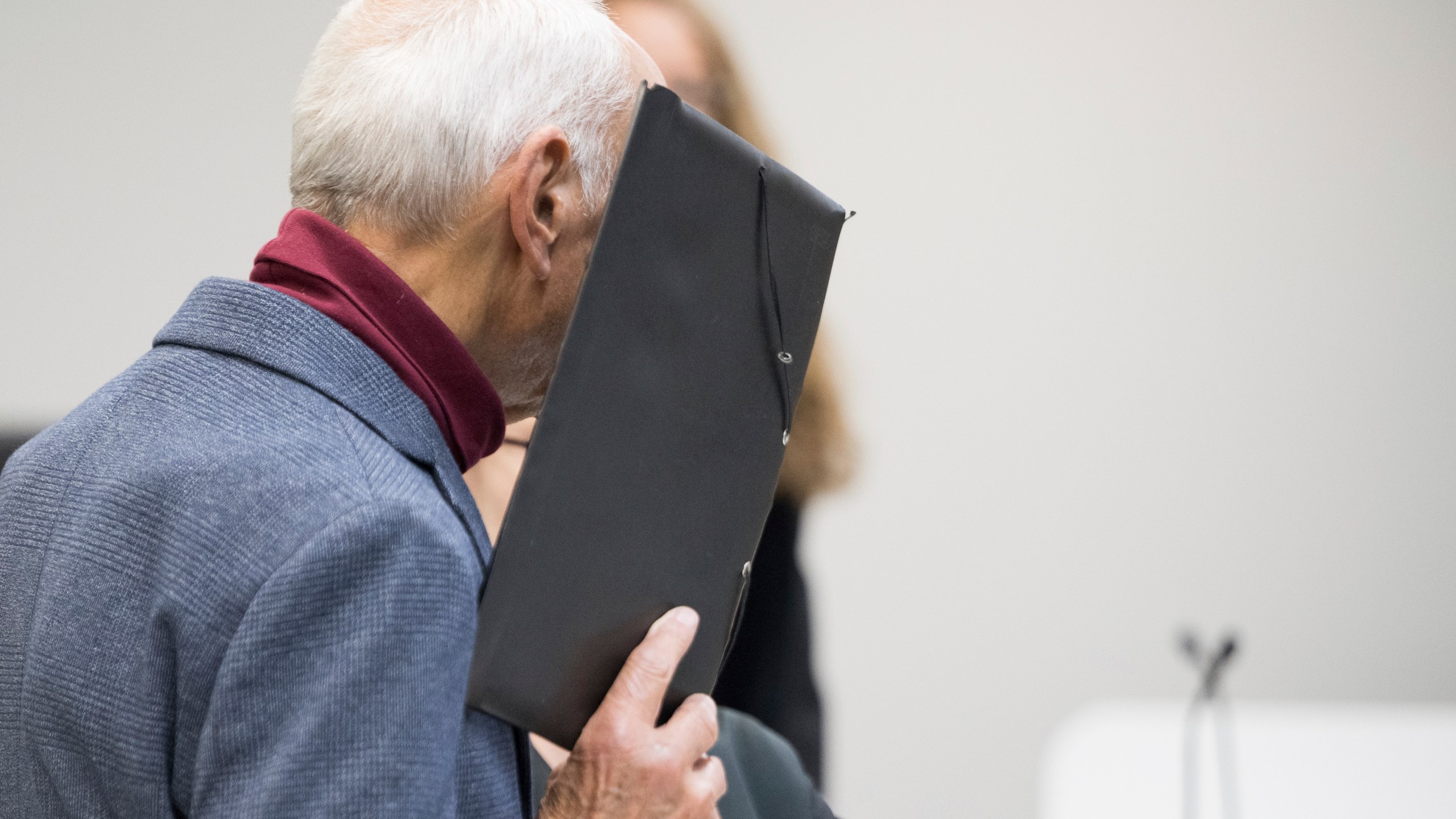 The defendant stands in front of the district court and covers his face before the verdict is announced in the trial against the ex-Stasi employee for murder of a Polish citizen at the former Berlin-Friedrichstraße border crossing in 1974, in Berlin, Monday, Oct. 14, 2024. (Sebastian Christoph Gollnow/dpa via AP)