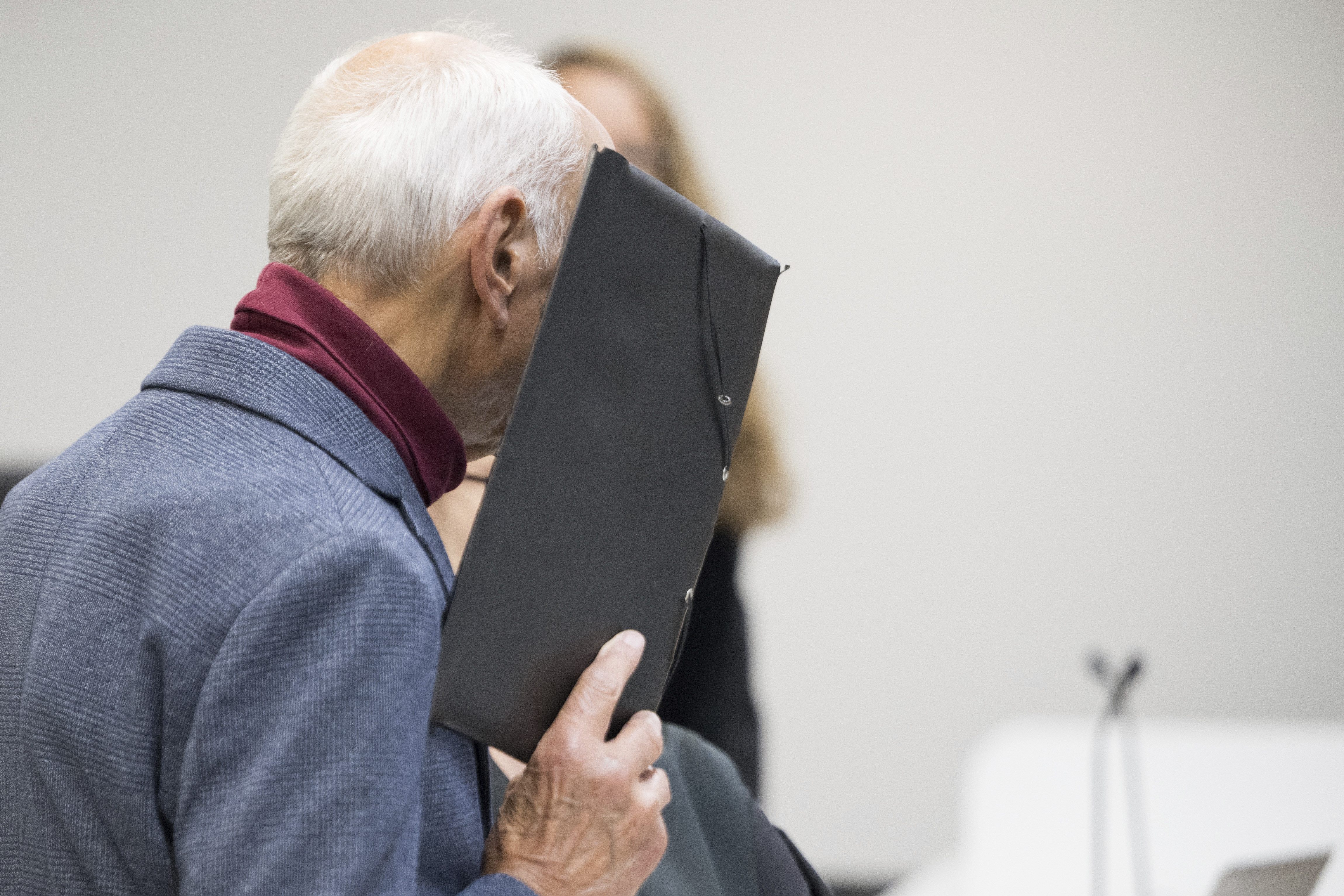 The defendant stands in front of the district court and covers his face before the verdict is announced in the trial against the ex-Stasi employee for murder of a Polish citizen at the former Berlin-Friedrichstraße border crossing in 1974, in Berlin, Monday, Oct. 14, 2024. (Sebastian Christoph Gollnow/dpa via AP)