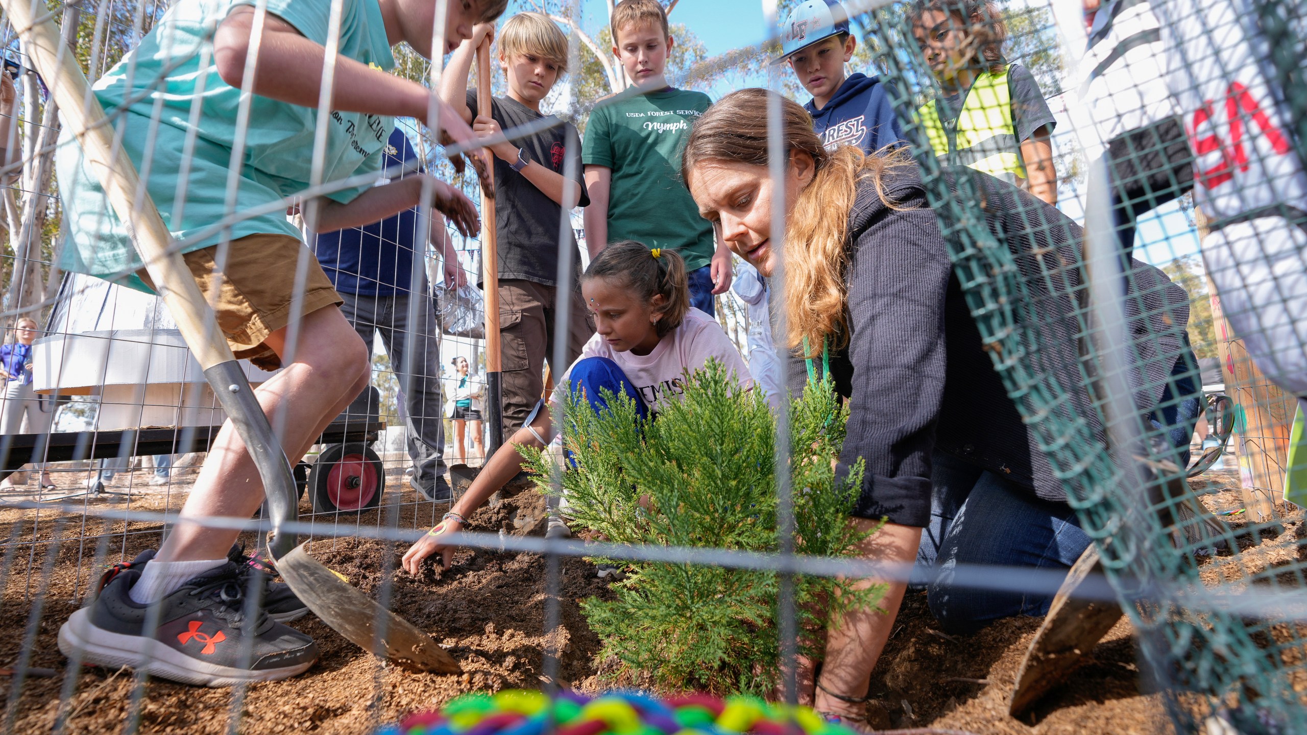 Santiago parent volunteer Stacie Aguesse, right, helps students plant a small Giant Sequoia tree from NASA's Artemis I Mission's tree seeds that traveled around the moon twice, as NASA scientists, JPL engineers, US Forest Service representatives, and teachers join Santiago STEAM Magnet Elementary School students at a ceremony to plant it after the school was honored in the spring of 2024 to become NASA Moon Tree Stewards in Lake Forest, Calif., on Monday, Oct. 14, 2024. (AP Photo/Damian Dovarganes)