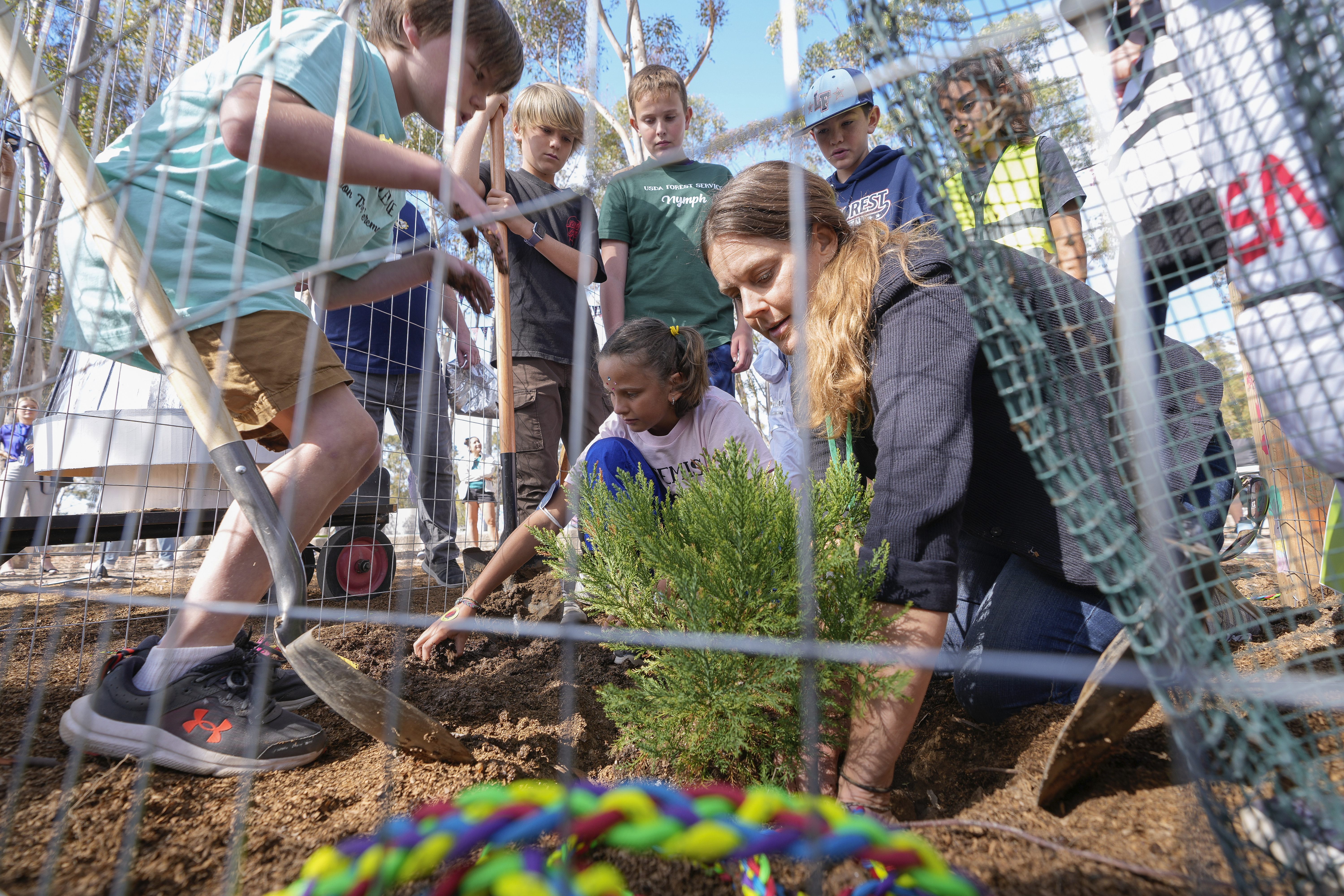 Santiago parent volunteer Stacie Aguesse, right, helps students plant a small Giant Sequoia tree from NASA's Artemis I Mission's tree seeds that traveled around the moon twice, as NASA scientists, JPL engineers, US Forest Service representatives, and teachers join Santiago STEAM Magnet Elementary School students at a ceremony to plant it after the school was honored in the spring of 2024 to become NASA Moon Tree Stewards in Lake Forest, Calif., on Monday, Oct. 14, 2024. (AP Photo/Damian Dovarganes)