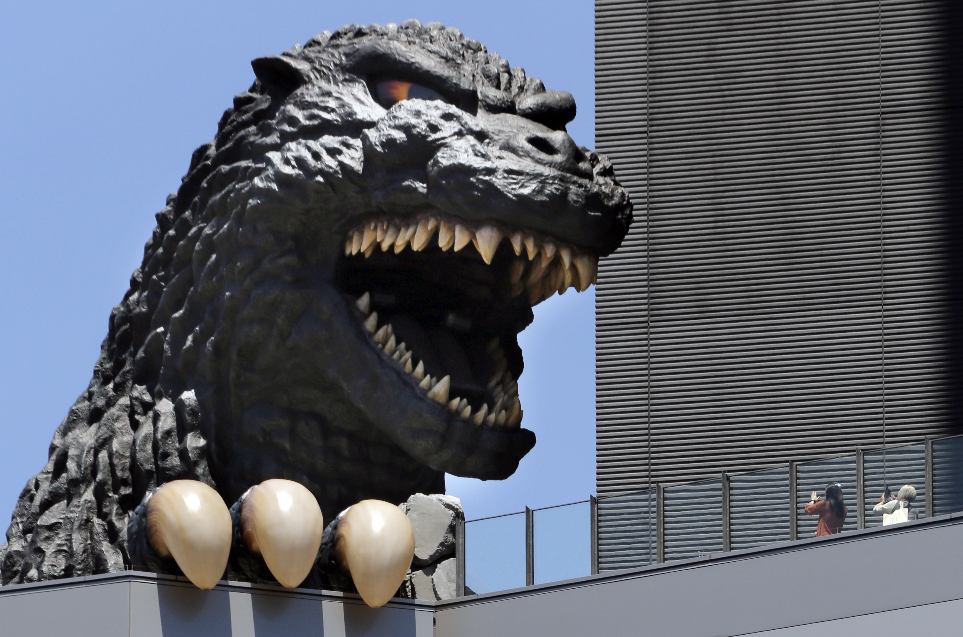 FILE - People take a picture of Godzilla's head at Shinjyuku Toho building at the Kabukicho district in Tokyo, July 30, 2016. (AP Photo/Koji Sasahara, File)