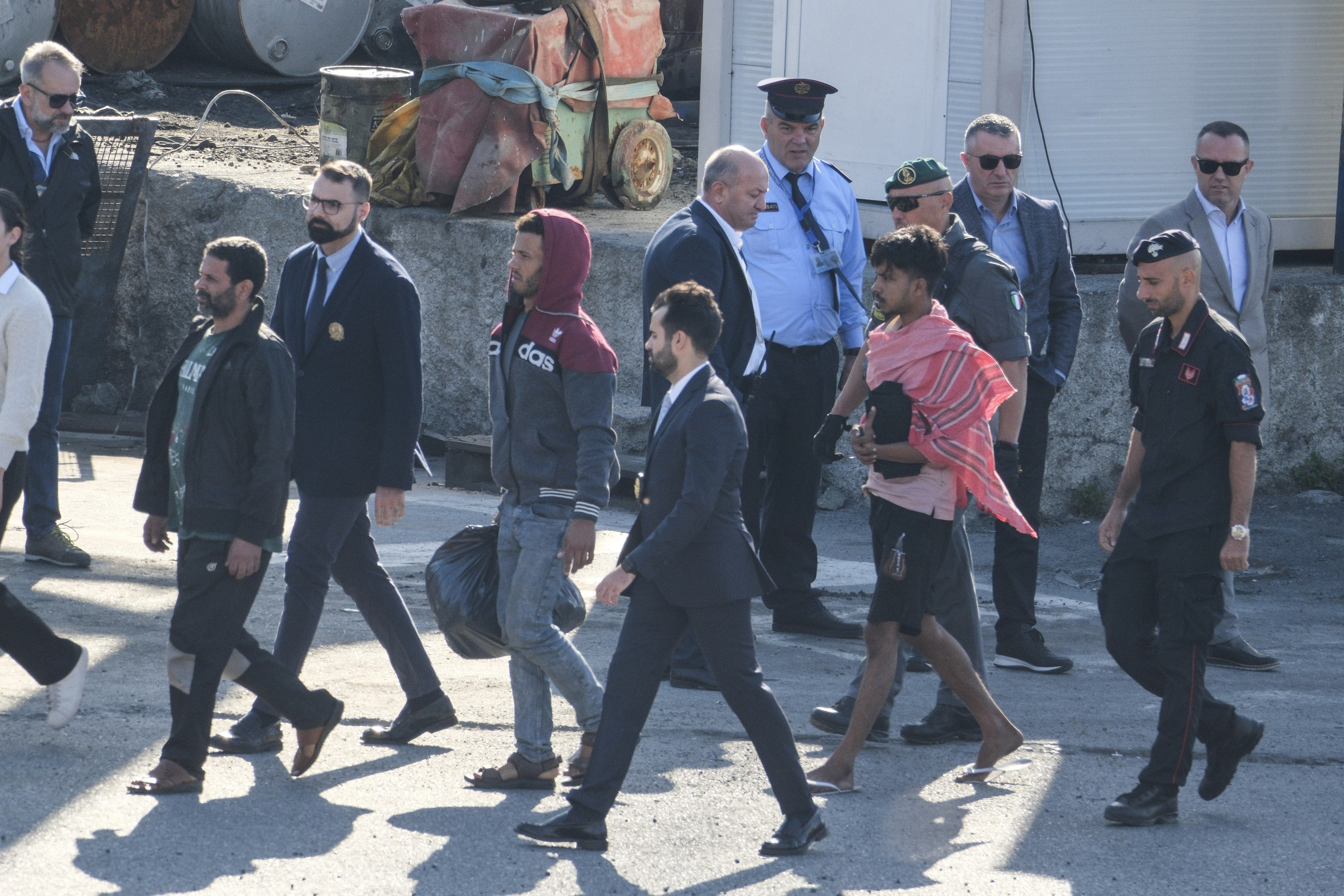 Migrant and security officials walk at the port of Shengjin, northwestern Albania. Wednesday, Oct. 16, 2024 after disembarking from the Italian navy ship Libra, carrying the first group of 16 migrants intercepted in international waters. (AP Photo/Vlasov Sulaj)