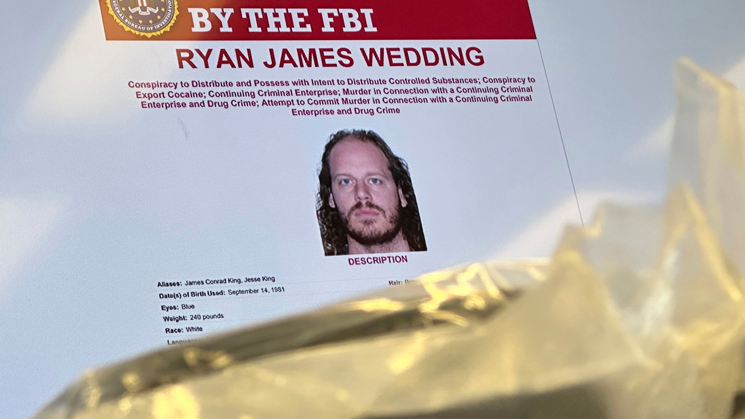 An image of former Canadian Olympic snowboarder Ryan Wedding, 43, who is a fugitive and been charged with allegedly running and participating in a transnational drug trafficking operation, is displayed on a video monitor along with bricks of cocaine, foreground, during a news conference at the FBI offices in Los Angeles, Thursday, Oct. 17, 2024. (AP Photo/Damian Dovarganes)