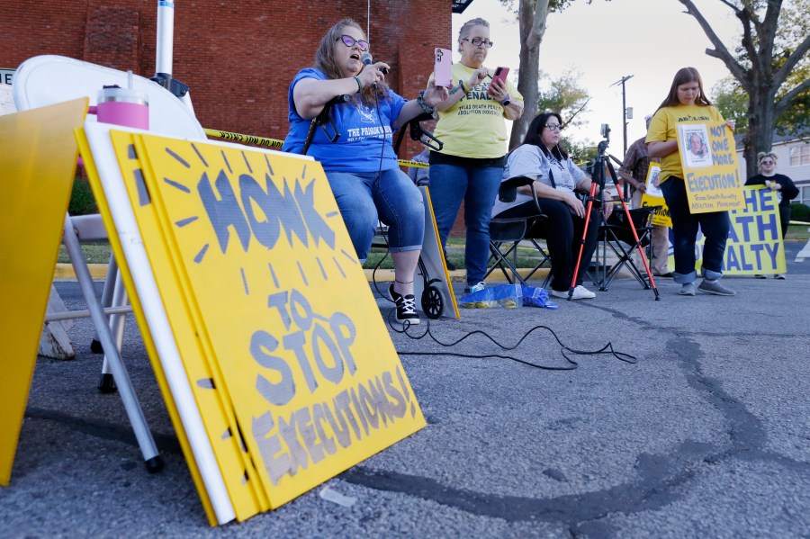 Dani Allen, center left with microphone, an anti-death penalty advocate, speaks during a protest outside the prison where Robert Roberson is scheduled for execution at the Huntsville Unit of the Texas State Penitentiary, Thursday, Oct. 17, 2024, in Huntsville, Texas. (AP Photo/Michael Wyke)