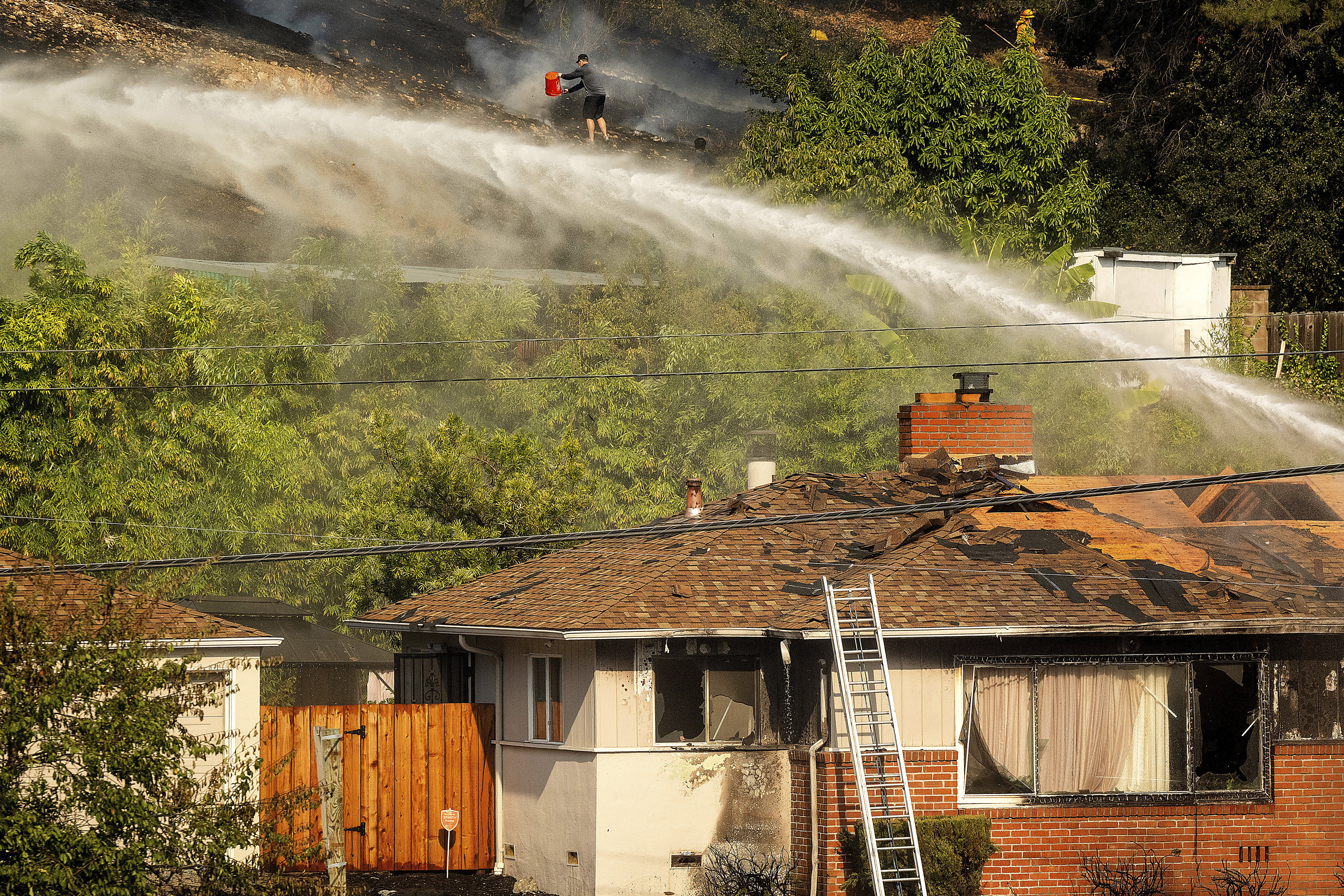 A person dumps water on a grass fire burning above Interstate 580 in Oakland, Calif., Friday, Oct. 18, 2024. (AP Photo/Noah Berger)