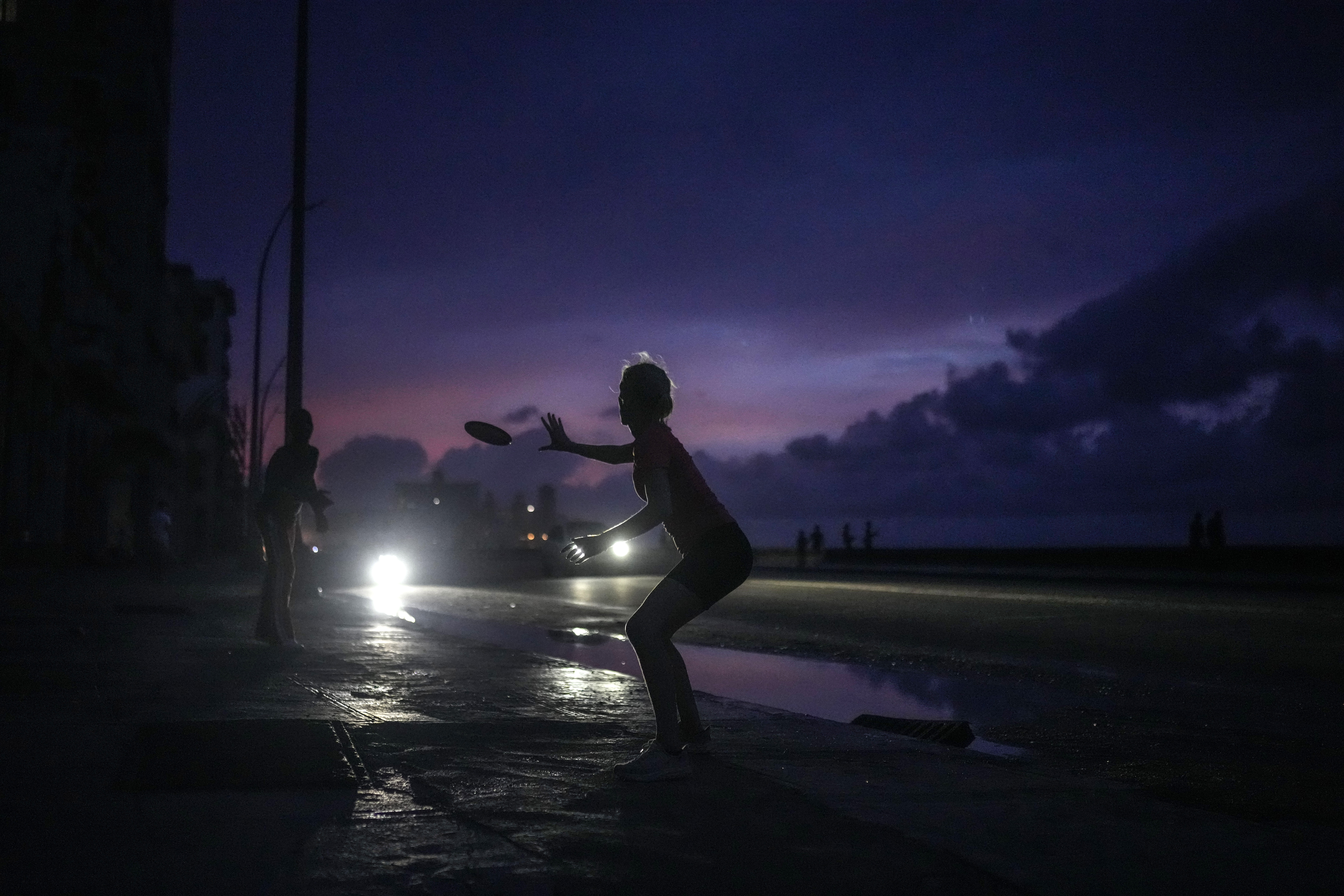 A woman prepares to catch a tossed frisbee during a massive blackout after a major power plant failed in Havana, Cuba, Friday, Oct. 18, 2024. (AP Photo/Ramon Espinosa)