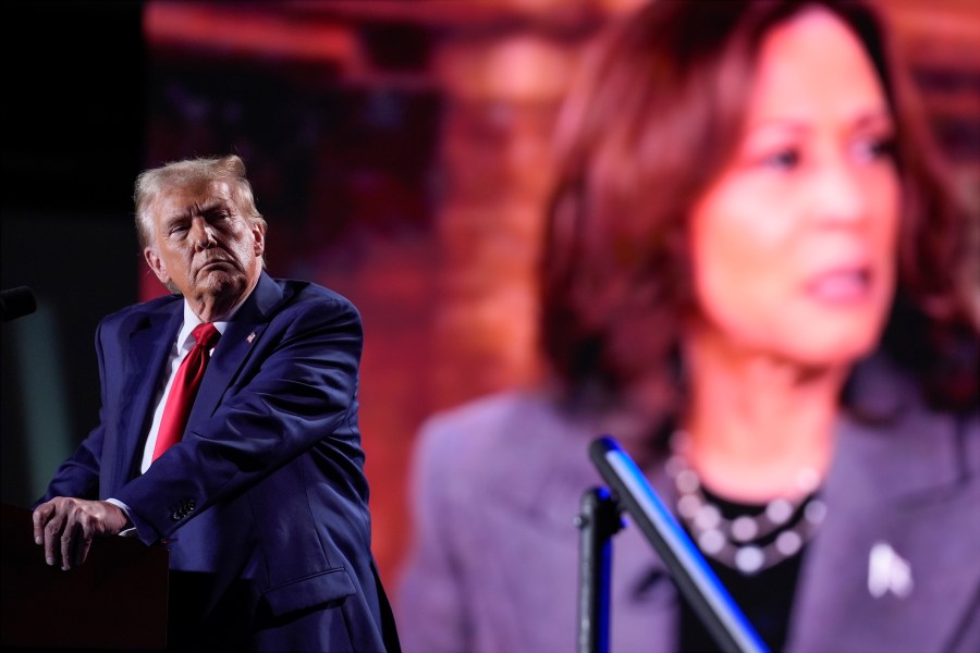 Republican presidential nominee former President Donald Trump watches a video on a screen with Democratic presidential nominee Vice President Kamala Harris as he speaks during a campaign event, Friday, Oct. 18, 2024 in Detroit. (AP Photo/Evan Vucci)