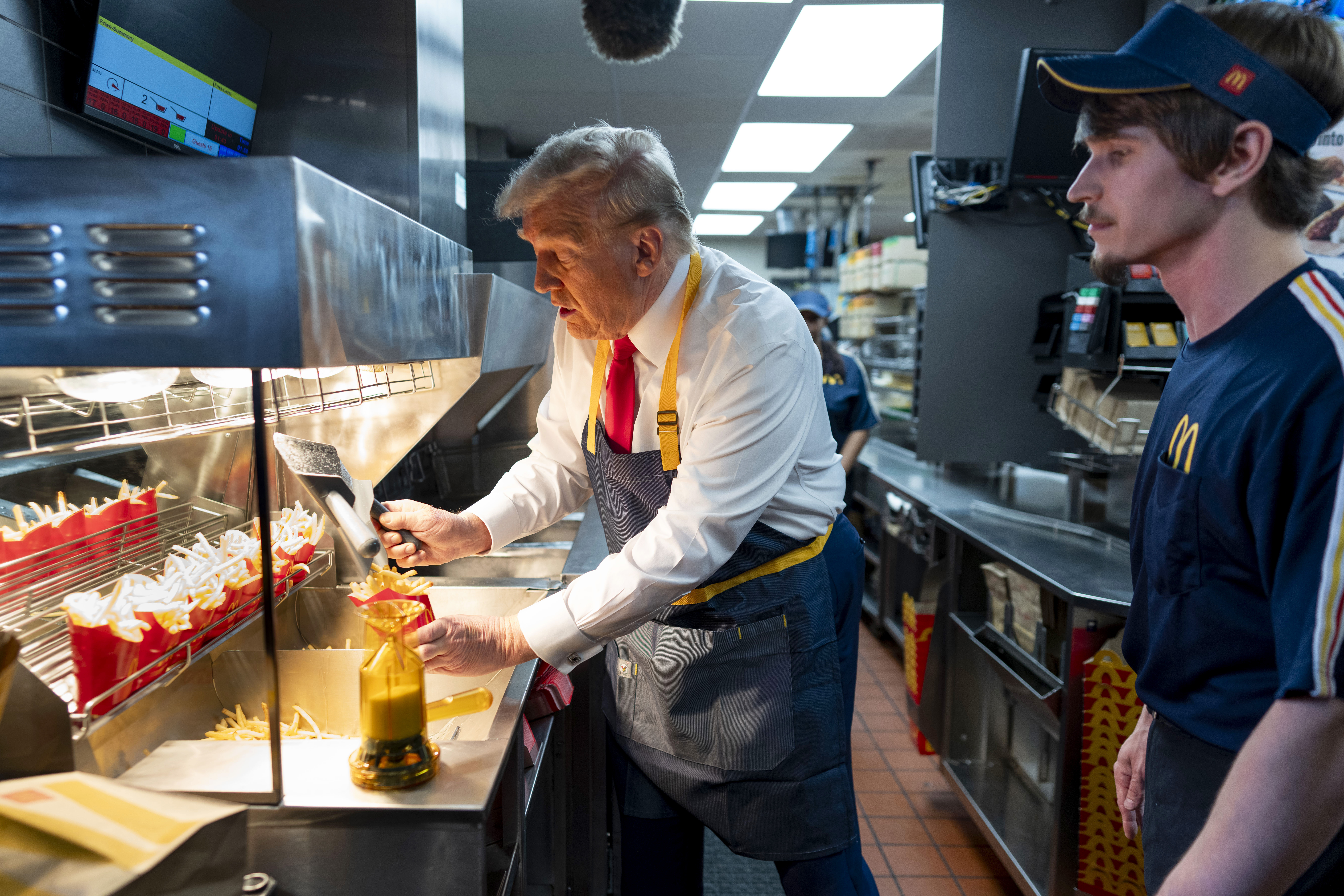 Republican presidential nominee former President Donald Trump, left, uses a frier as an employee looks on during a visit to McDonald's in Feasterville-Trevose, Pa., Sunday, Oct. 20, 2024. (Doug Mills/The New York Times via AP, Pool)