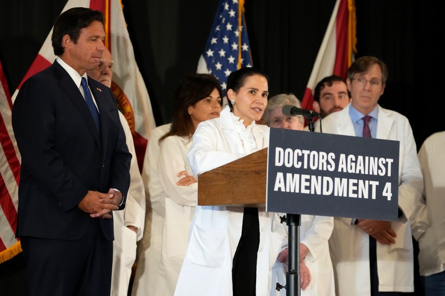 Dr. Christina Pena speaks during a news conference with Florida Physicians Against Amendment 4 as Florida Gov. Ron DeSantis, left, looks on Monday, Oct. 21, 2024, in Coral Gables, Fla. (AP Photo/Lynne Sladky)