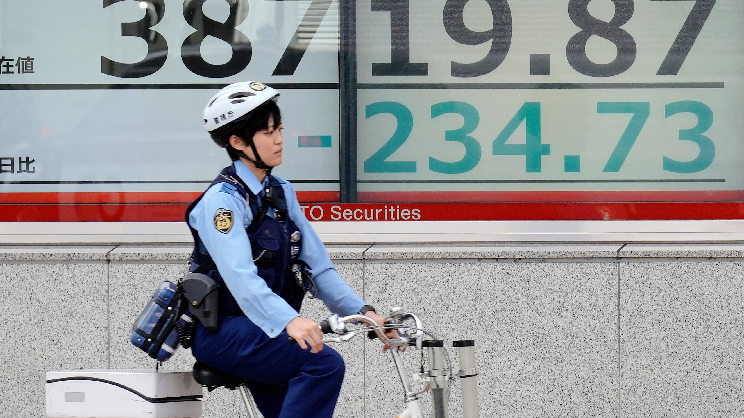 A police officer rides a bicycle in front of an electronic stock board showing Japan's Nikkei index at a securities firm Tuesday, Oct. 22, 2024, in Tokyo. (AP Photo/Eugene Hoshiko)