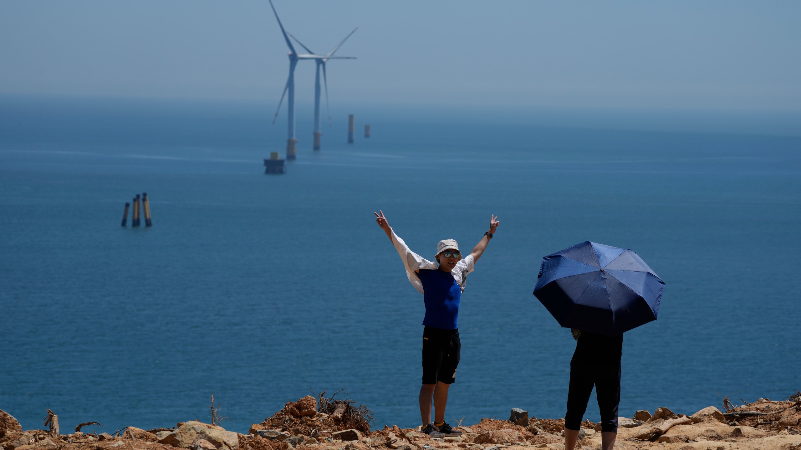 FILE - A tourist poses for photos near turbines along the Taiwan Straits in Pingtan in eastern China's Fujian province, on Aug. 6, 2022. (AP Photo/Ng Han Guan, File)