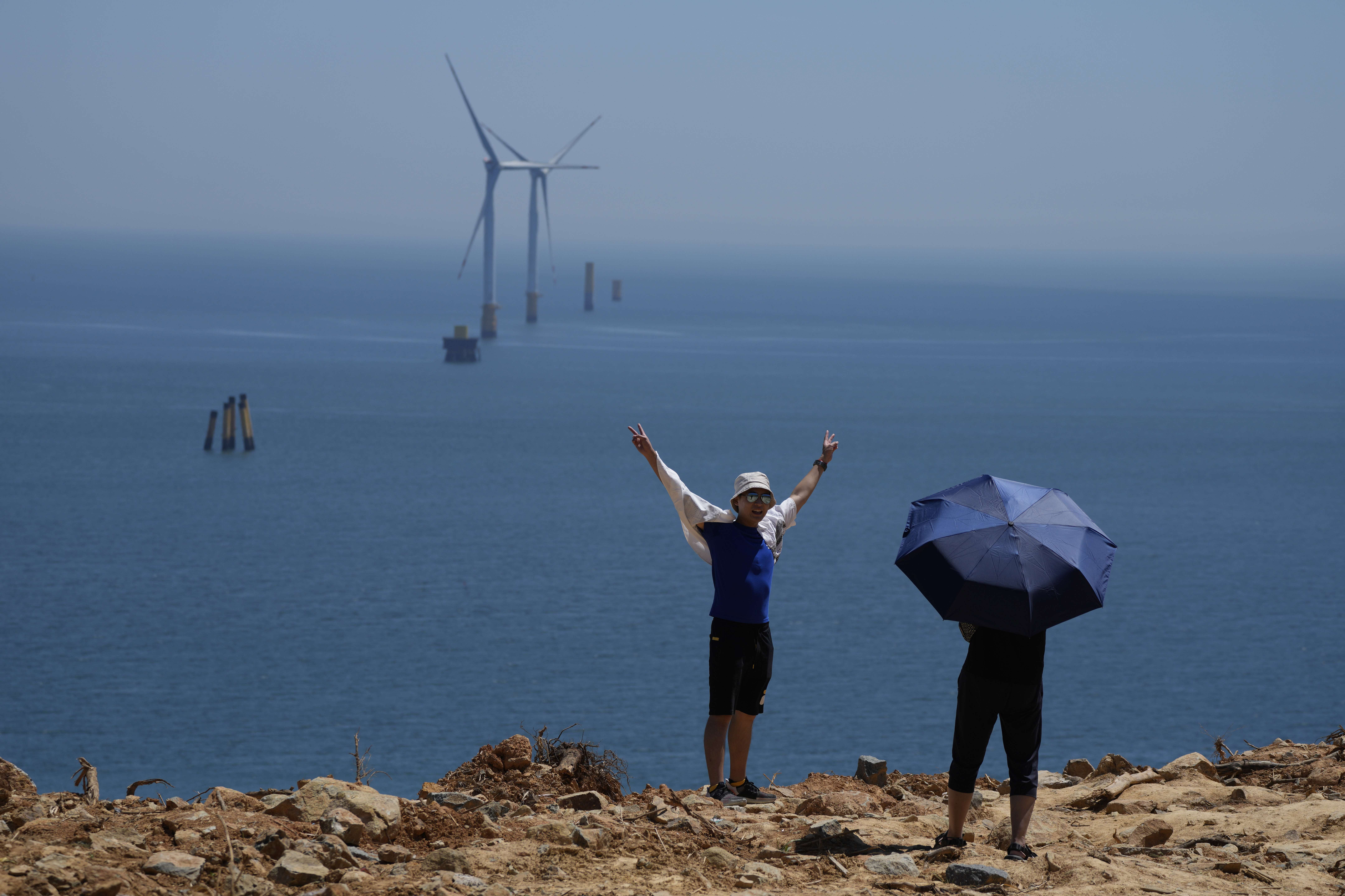 FILE - A tourist poses for photos near turbines along the Taiwan Straits in Pingtan in eastern China's Fujian province, on Aug. 6, 2022. (AP Photo/Ng Han Guan, File)