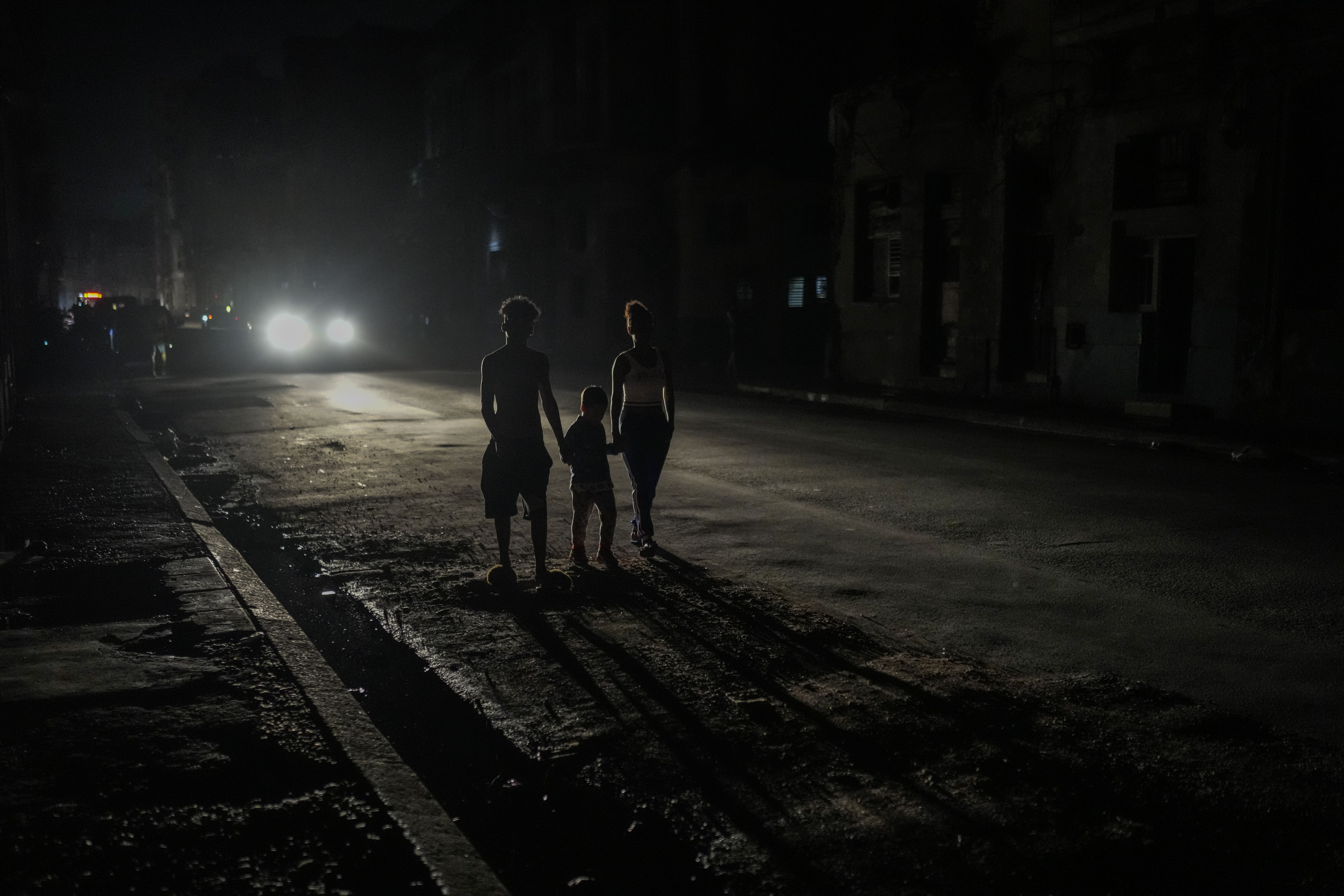 FILE - Residents are illuminated by the headlights of a car during a blackout after a major power plant failed in Havana, Cuba, Oct. 18, 2024. (AP Photo/Ramon Espinosa, File)