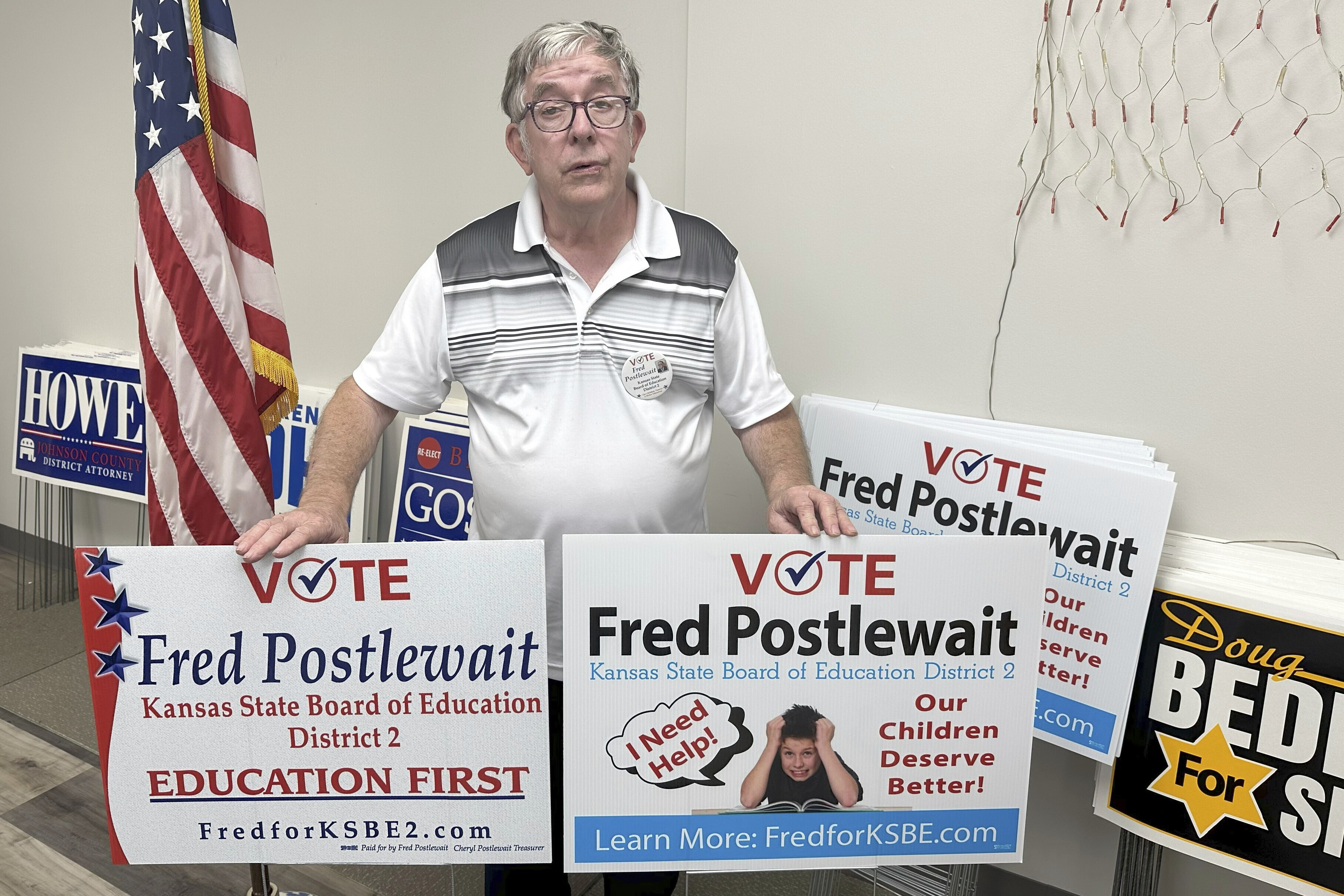 Fred Postlewait, a Republican candidate for the Kansas State Board of Education from Kansas City, Kan., shows off two of the yard signs available for supporters at the Republican Party's local headquarters in Johnson County, Tuesday, Oct. 1, 2024, in Overland Park, Kan. (AP Photo/John Hanna)