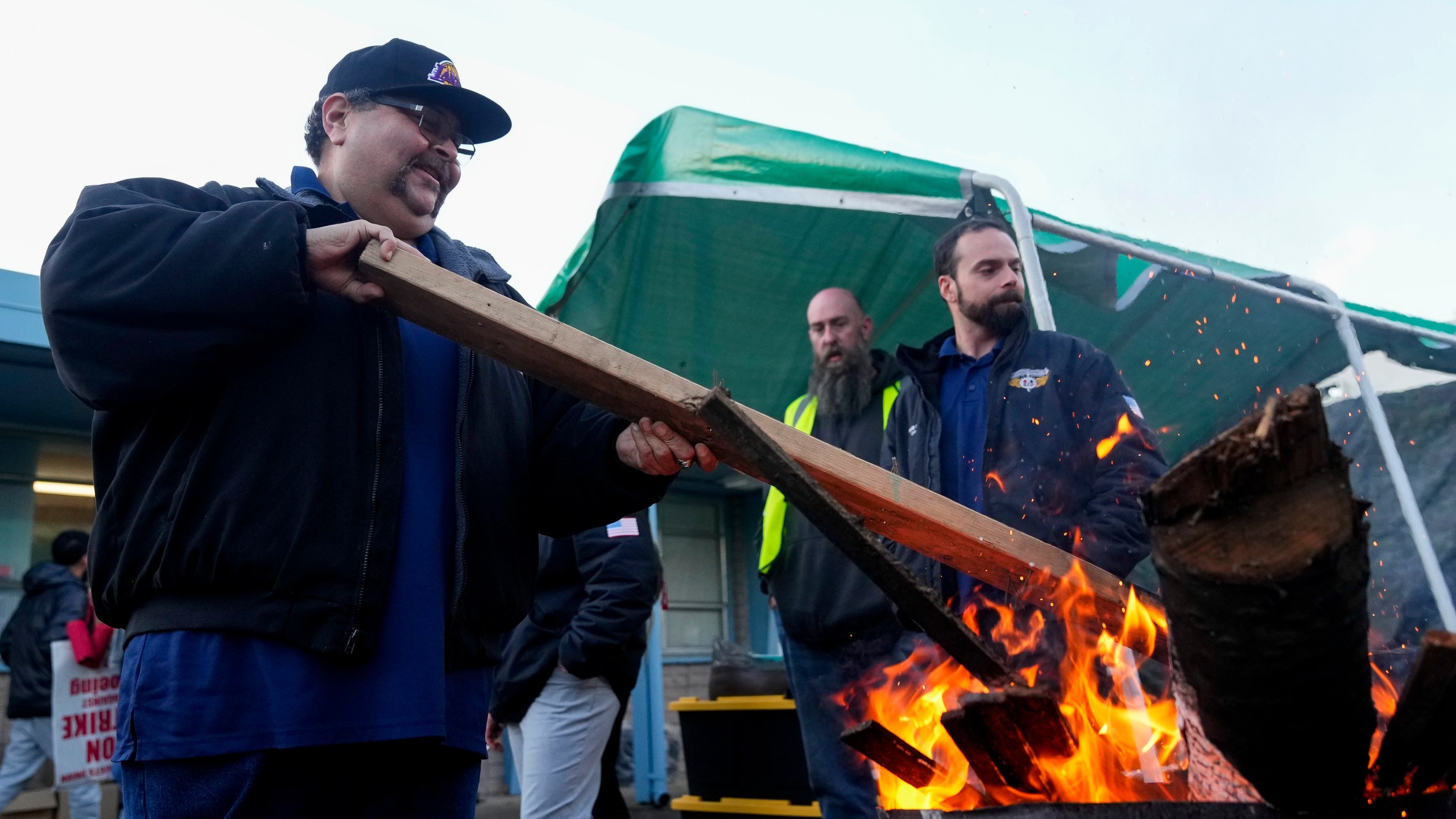 Boeing employee Adrian Camez, who works in Seattle, stokes the fire of a burn barrel as others arrive to vote on a new contract offer from the company Monday, Nov. 4, 2024, at the Aerospace Machinists Union hall in Renton, Wash. (AP Photo/Lindsey Wasson)