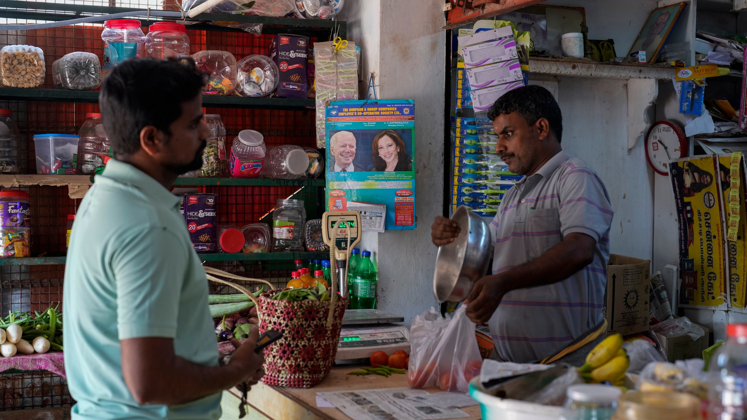 Manikandan Ganesan, right, a local shopkeeper, packs vegetables for a customer at his grocery store outside Sri Dharmasastha Hindu temple in Thulasendrapuram, the ancestral village of Democratic presidential nominee Vice President Kamala Harris, in Tamil Nadu state, India, Monday, Nov. 4, 2024. (AP Photo/Aijaz Rahi)