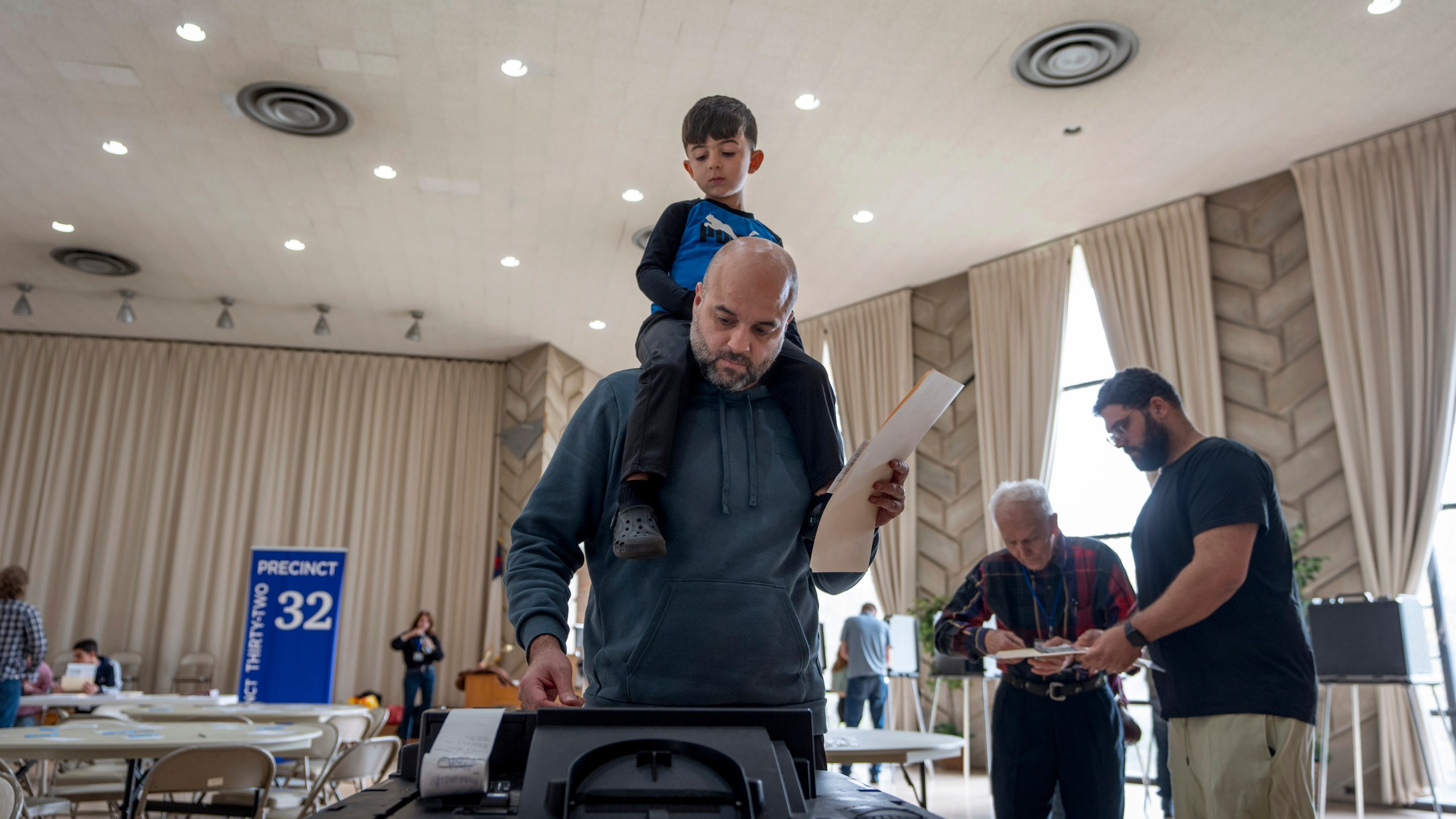 Three-year-old Zayn, sits on his father's shoulders as he inserts his ballot into a machine to vote at the First Presbyterian Church of Dearborn, on Election Day, Tuesday, Nov. 5, 2024, in Dearborn, Mich. (AP Photo/David Goldman)