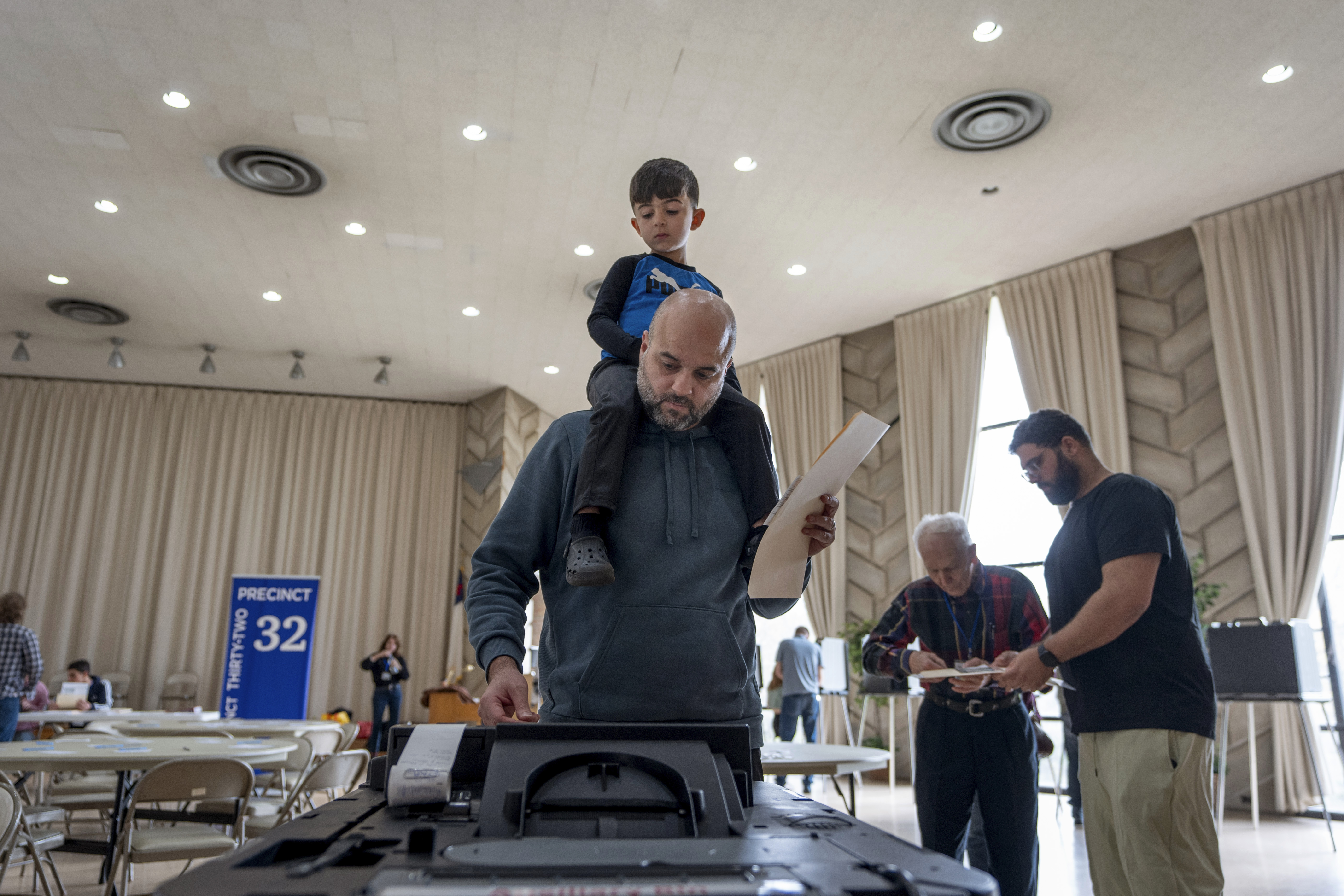 Three-year-old Zayn, sits on his father's shoulders as he inserts his ballot into a machine to vote at the First Presbyterian Church of Dearborn, on Election Day, Tuesday, Nov. 5, 2024, in Dearborn, Mich. (AP Photo/David Goldman)