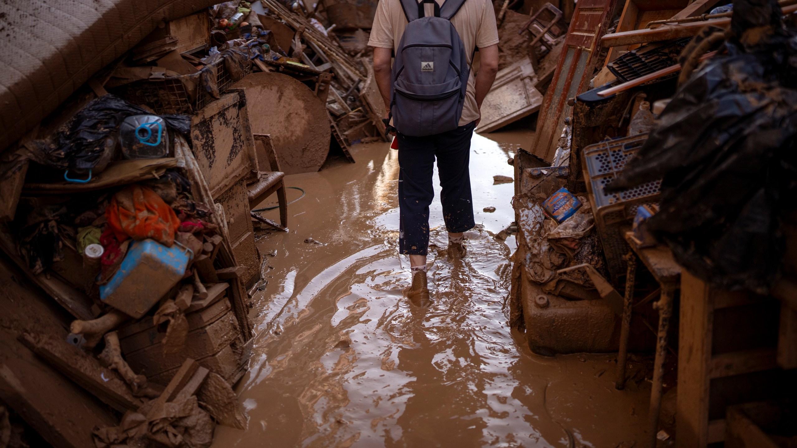 A person walks through a street with piled furniture and rubbish on the sides, in an area affected by floods in Paiporta, Valencia, Spain, Tuesday, Nov. 5, 2024. (AP Photo/Emilio Morenatti)