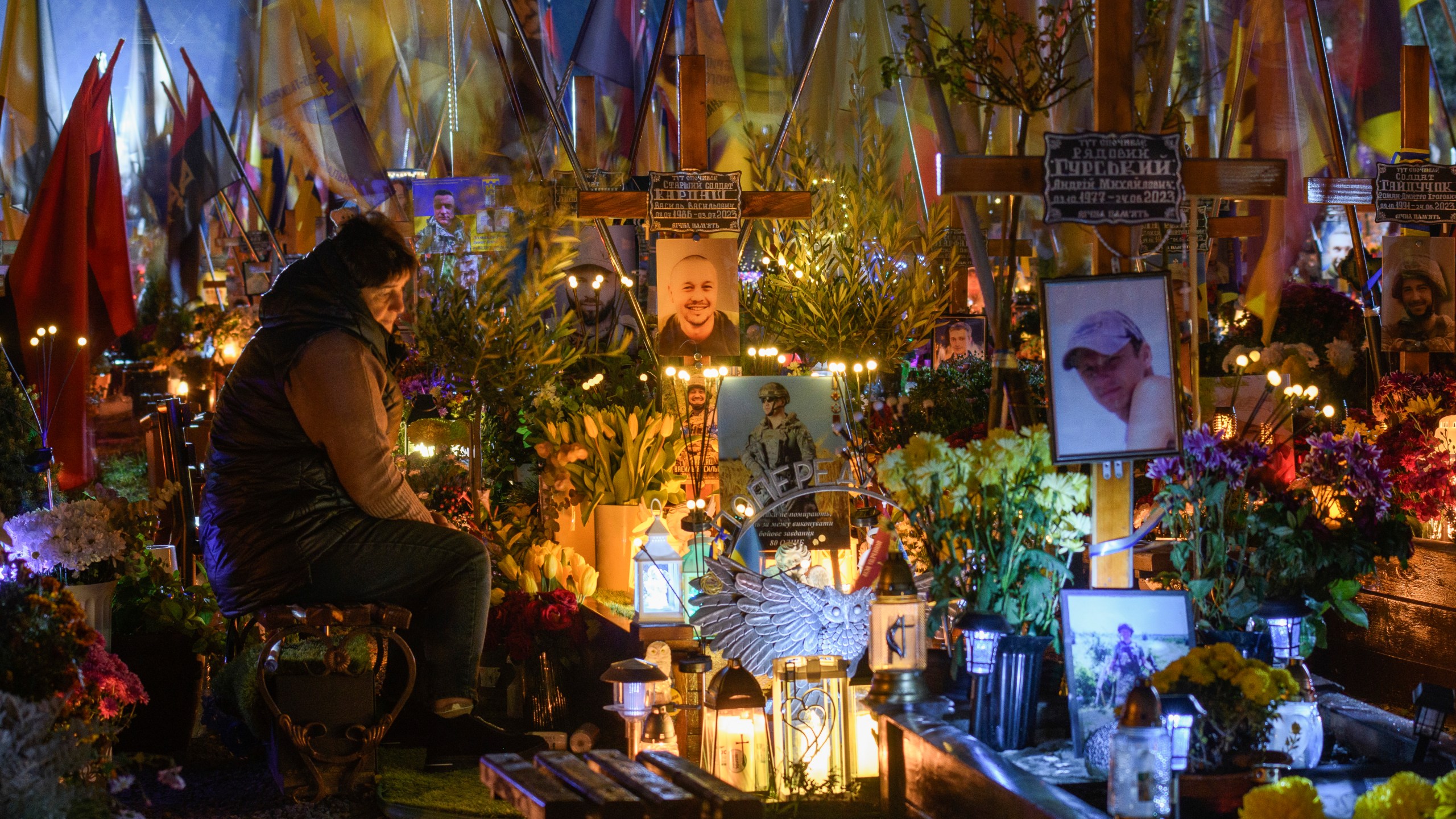 A relative lit candles and brings flowers and flags at the graves of the Ukrainian soldiers who died in the war with Russia on All Saints' Day on the Mars Field at Lychakiv cemetery in Lviv, Ukraine, Friday, Nov. 1, 2024. (AP Photo/Mykola Tys)