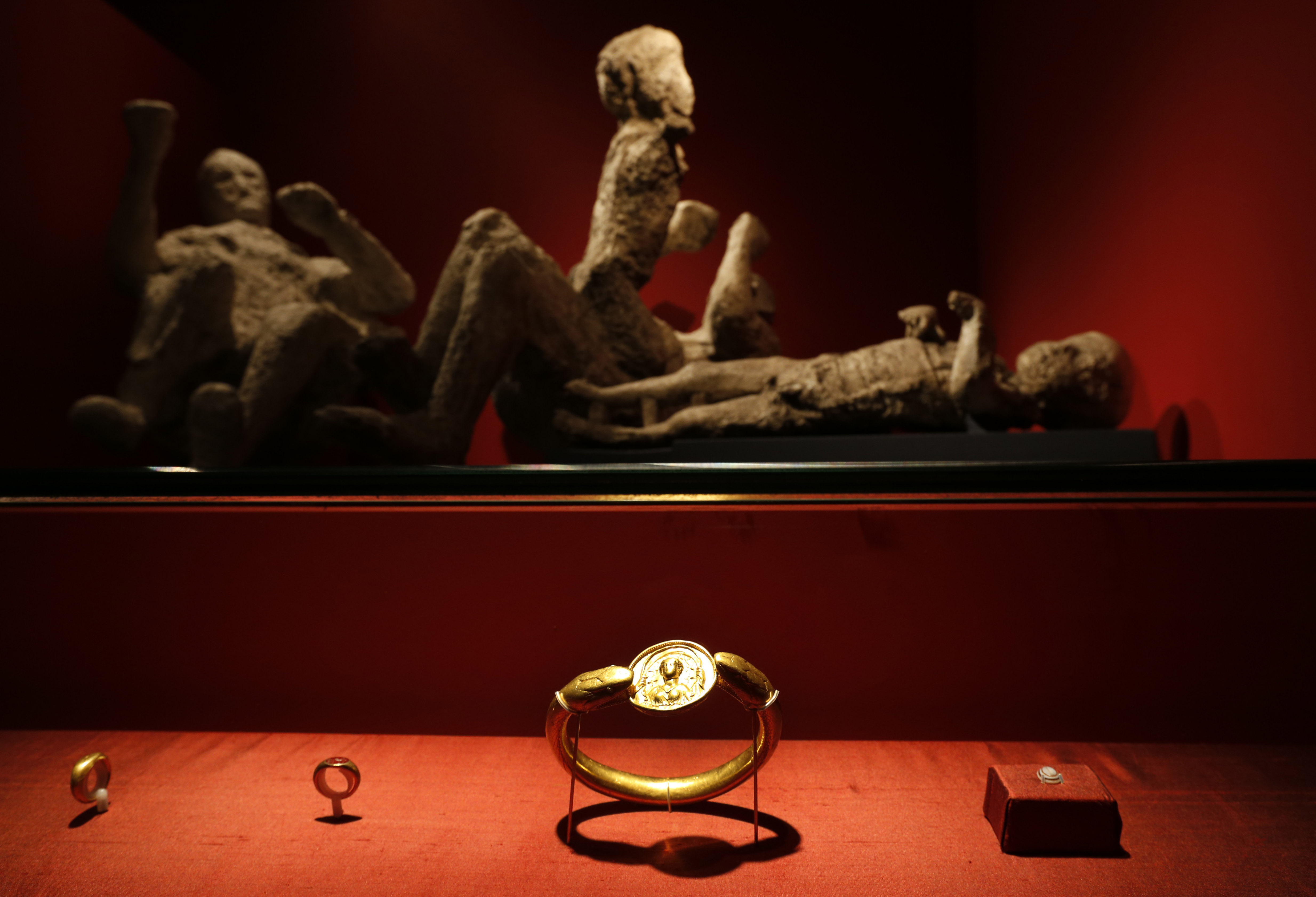 FILE - Jewelry found in the ruins of a house in Pompeii are displayed, backdropped by the casts of two adults and two children who died together in the house in Pompeii, at the exhibition, "Life and death Pompeii and Herculaneum," at the British Museum in central London, March 26, 2013. (AP Photo/Lefteris Pitarakis, File)