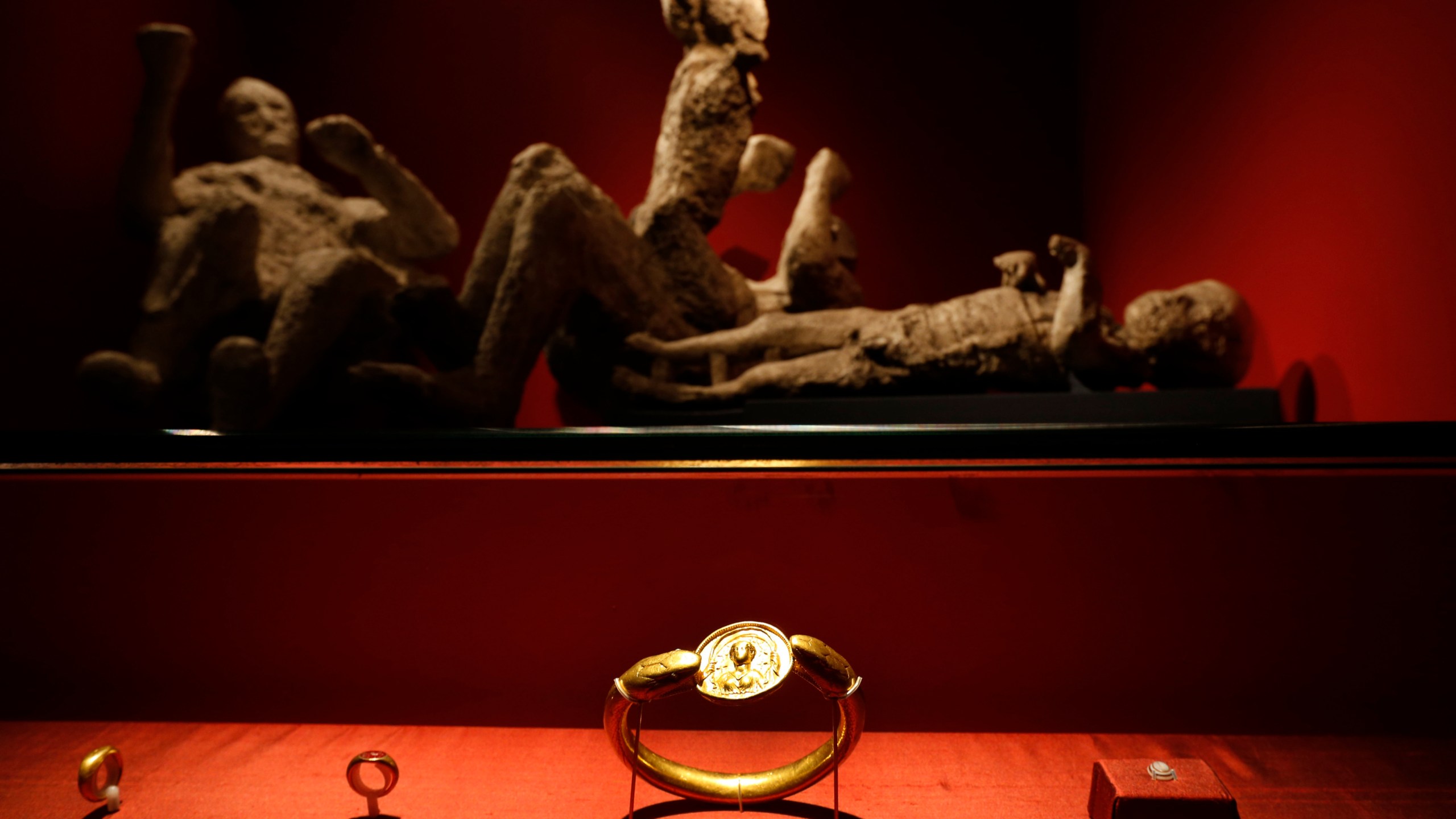 FILE - Jewelry found in the ruins of a house in Pompeii are displayed, backdropped by the casts of two adults and two children who died together in the house in Pompeii, at the exhibition, "Life and death Pompeii and Herculaneum," at the British Museum in central London, March 26, 2013. (AP Photo/Lefteris Pitarakis, File)