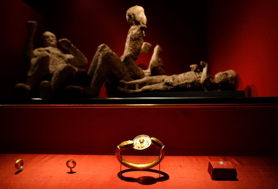 FILE - Jewelry found in the ruins of a house in Pompeii are displayed, backdropped by the casts of two adults and two children who died together in the house in Pompeii, at the exhibition, "Life and death Pompeii and Herculaneum," at the British Museum in central London, March 26, 2013. (AP Photo/Lefteris Pitarakis, File)