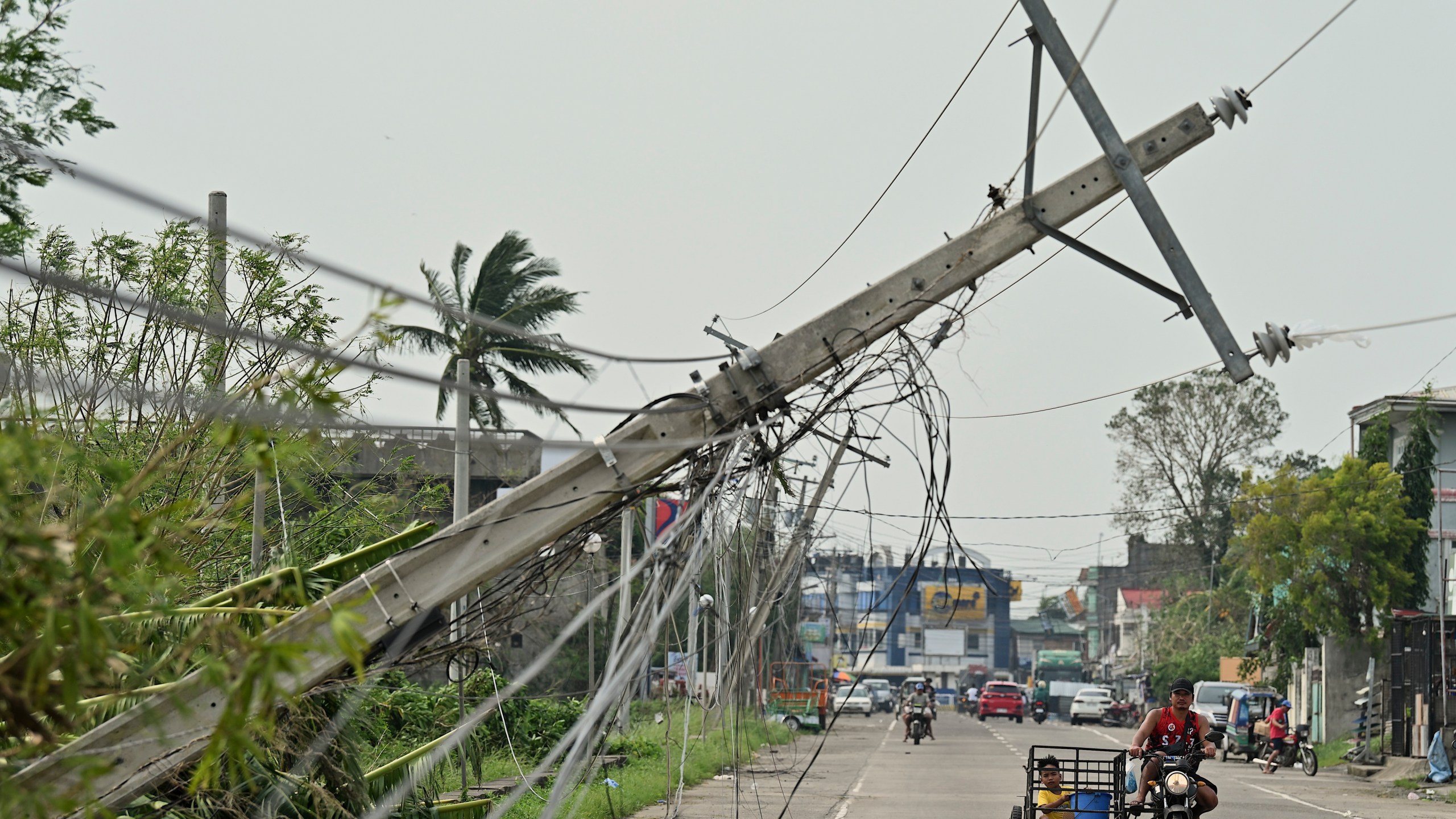 Residents riding a tricycle pass by toppled electrical post caused by Typhoon Yinxing, locally called Marce, in Camalaniugan, Cagayan province, northern Philippines on Friday, Nov. 8, 2024. (AP Photo/Noel Celis)