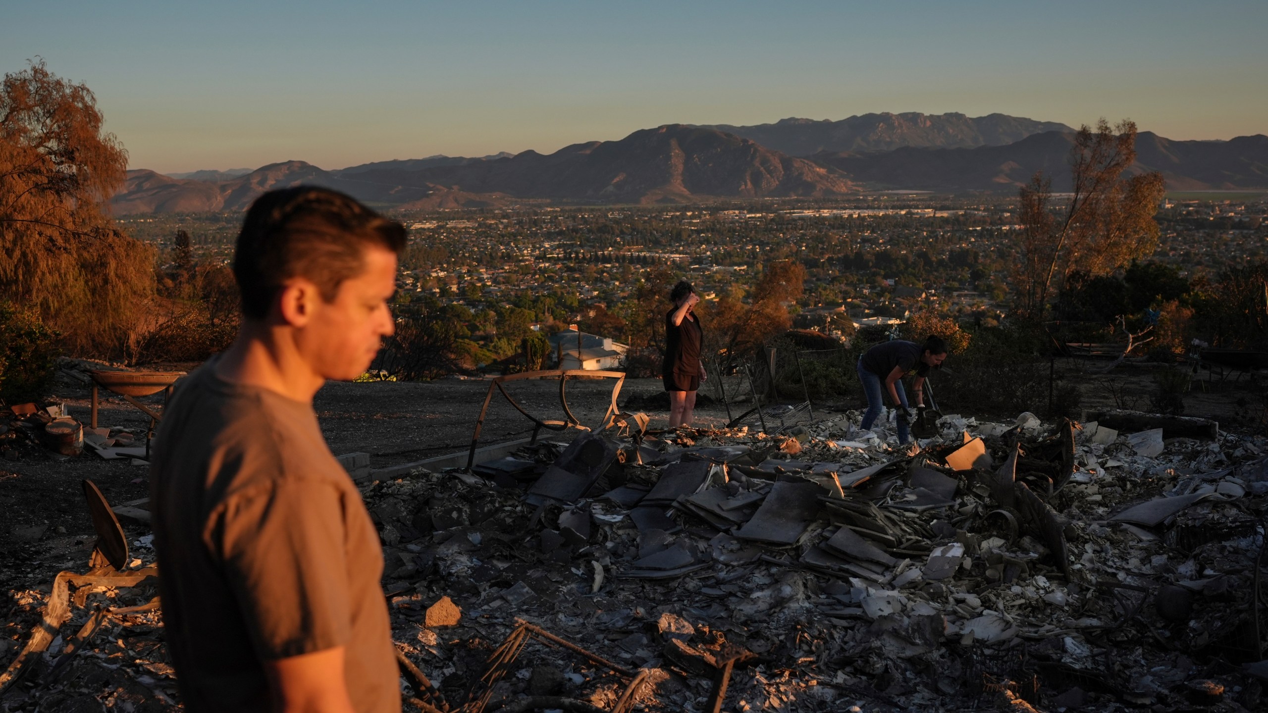 Louie Gonzalez, foreground, and his mother, Kathy, background center, visit Kathy's home devastated in the Mountain Fire in Camarillo, Calif., Nov. 8, 2024. (AP Photo/Jae C. Hong)