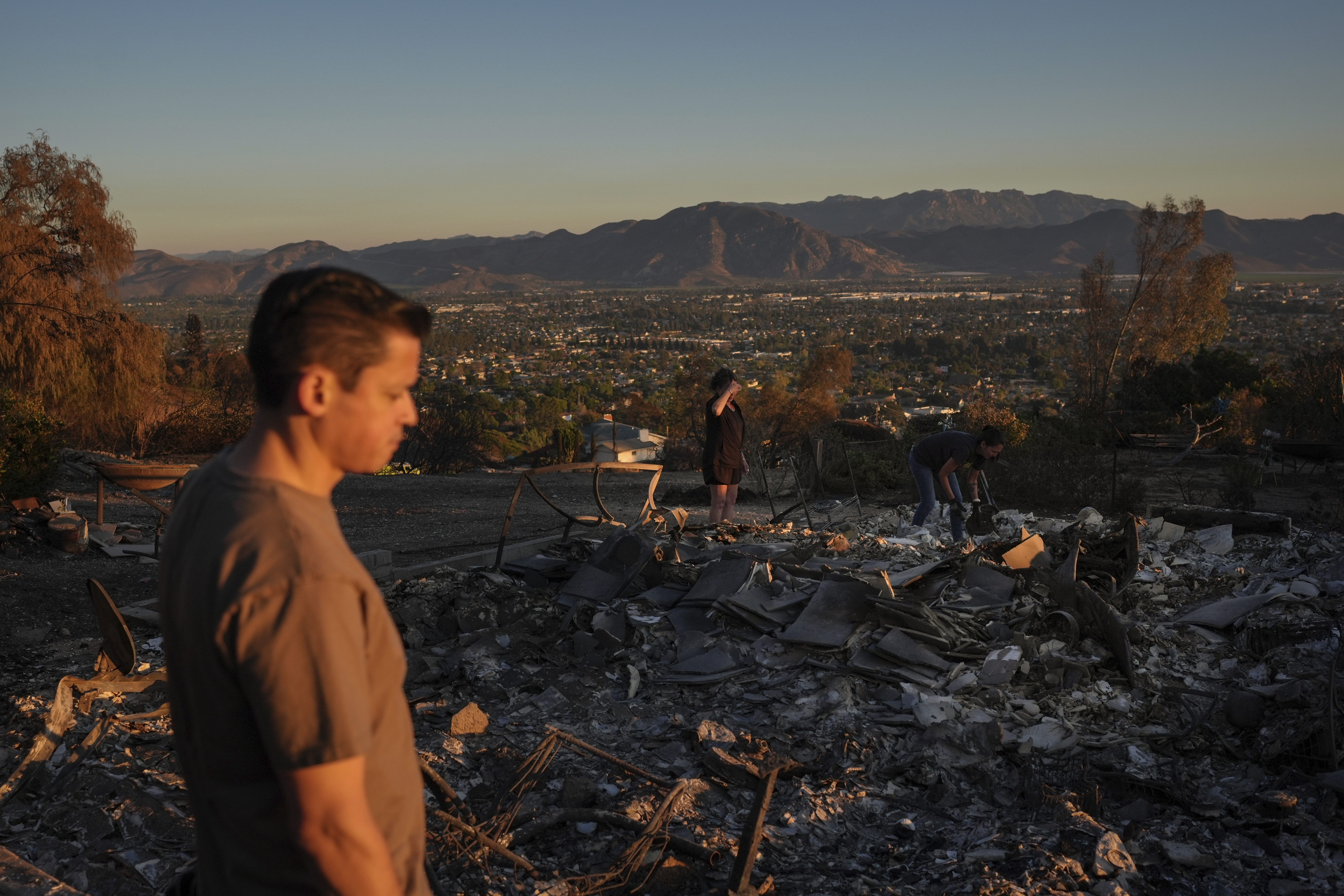 Louie Gonzalez, foreground, and his mother, Kathy, background center, visit Kathy's home devastated in the Mountain Fire in Camarillo, Calif., Nov. 8, 2024. (AP Photo/Jae C. Hong)