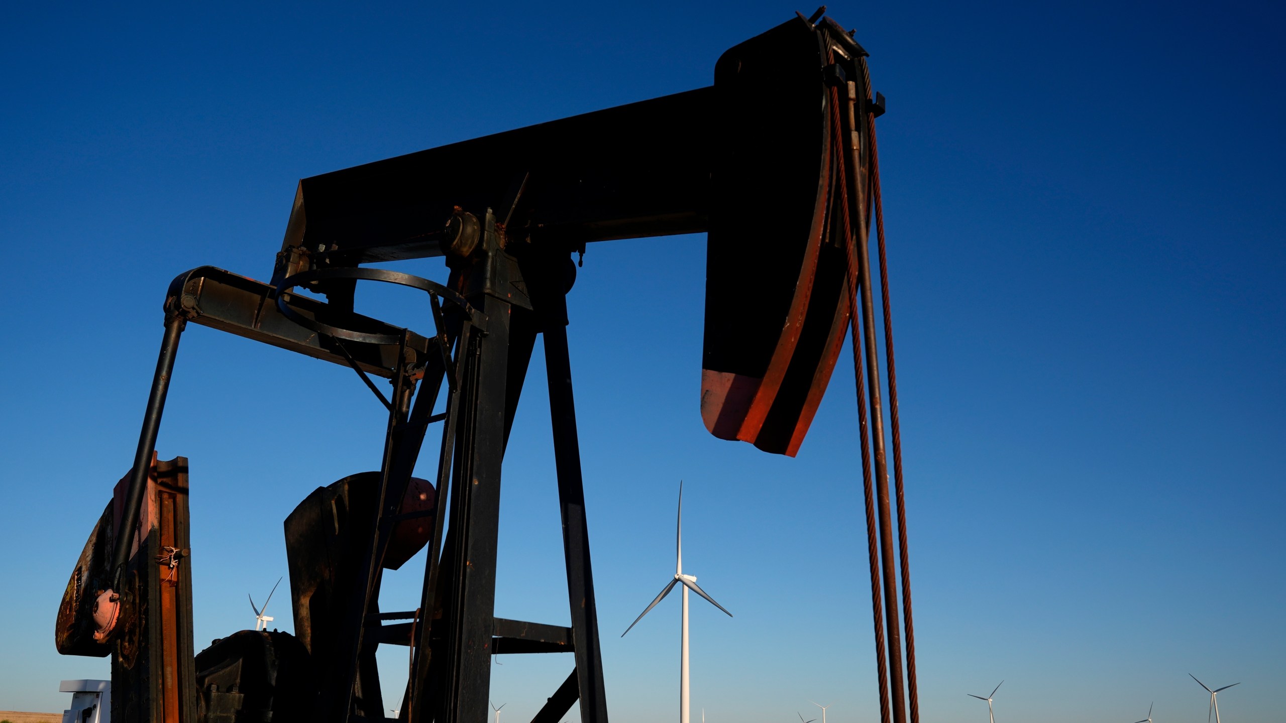 A pumpjack operates in the foreground as wind turbines at the Buckeye Wind Energy wind farm rise in the distance, Monday, Sept. 30, 2024, near Hays, Kan. (AP Photo/Charlie Riedel)