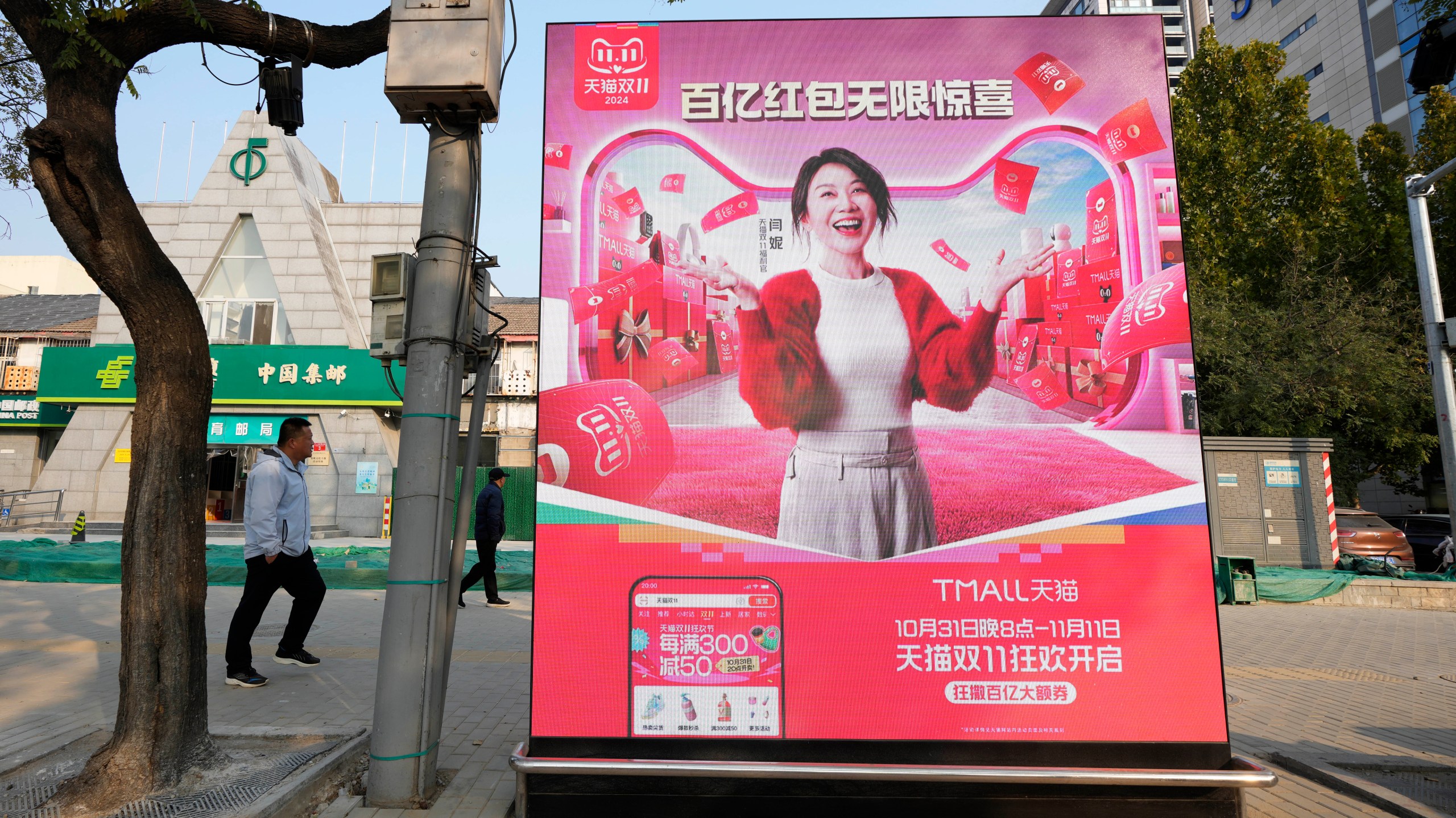 Pedestrians walk near an advertisement promoting a sales festival in Beijing, Thursday, Nov. 7, 2024. (AP Photo/Ng Han Guan)