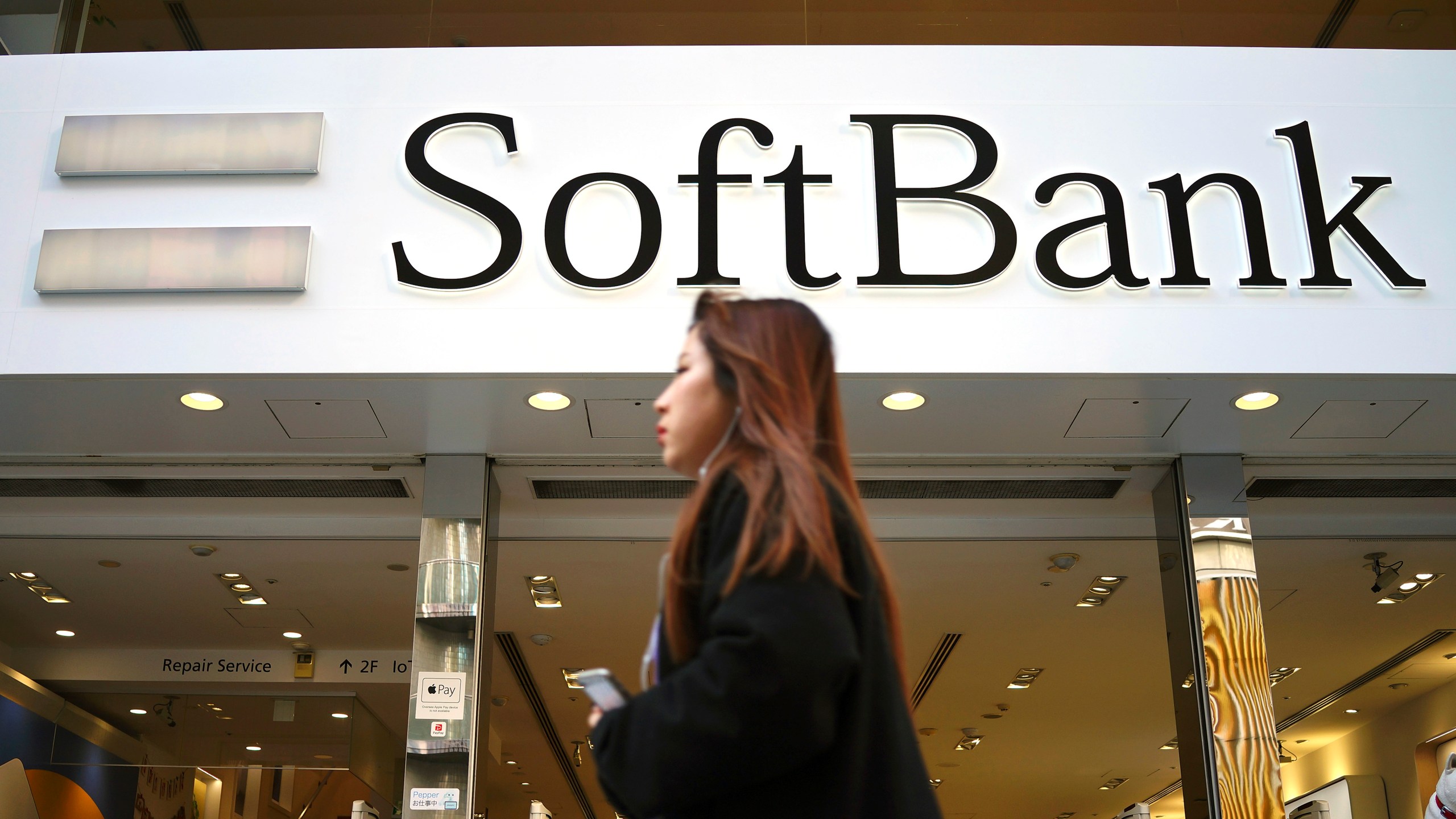 FILE - A woman walks in front of SoftBank store in Ginza shopping district in Tokyo, Jan. 20, 2020. (AP Photo/Eugene Hoshiko, File)